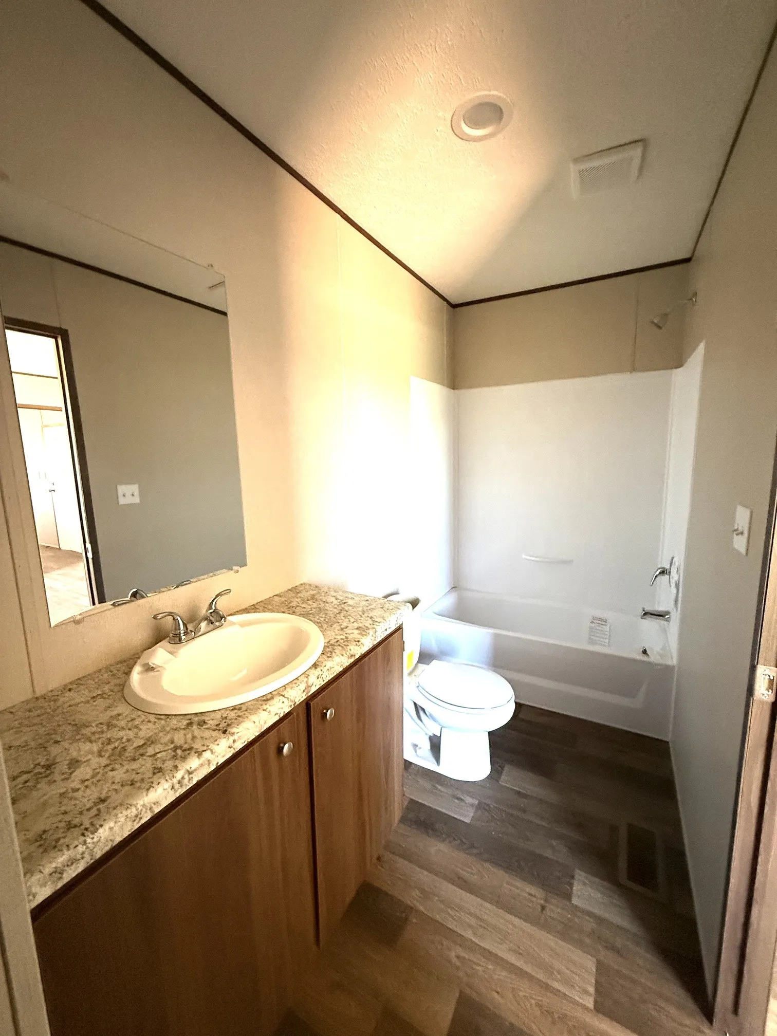 Bathroom featuring a wood-finish vanity with a light speckled countertop, an oval undermount sink, and a chrome faucet