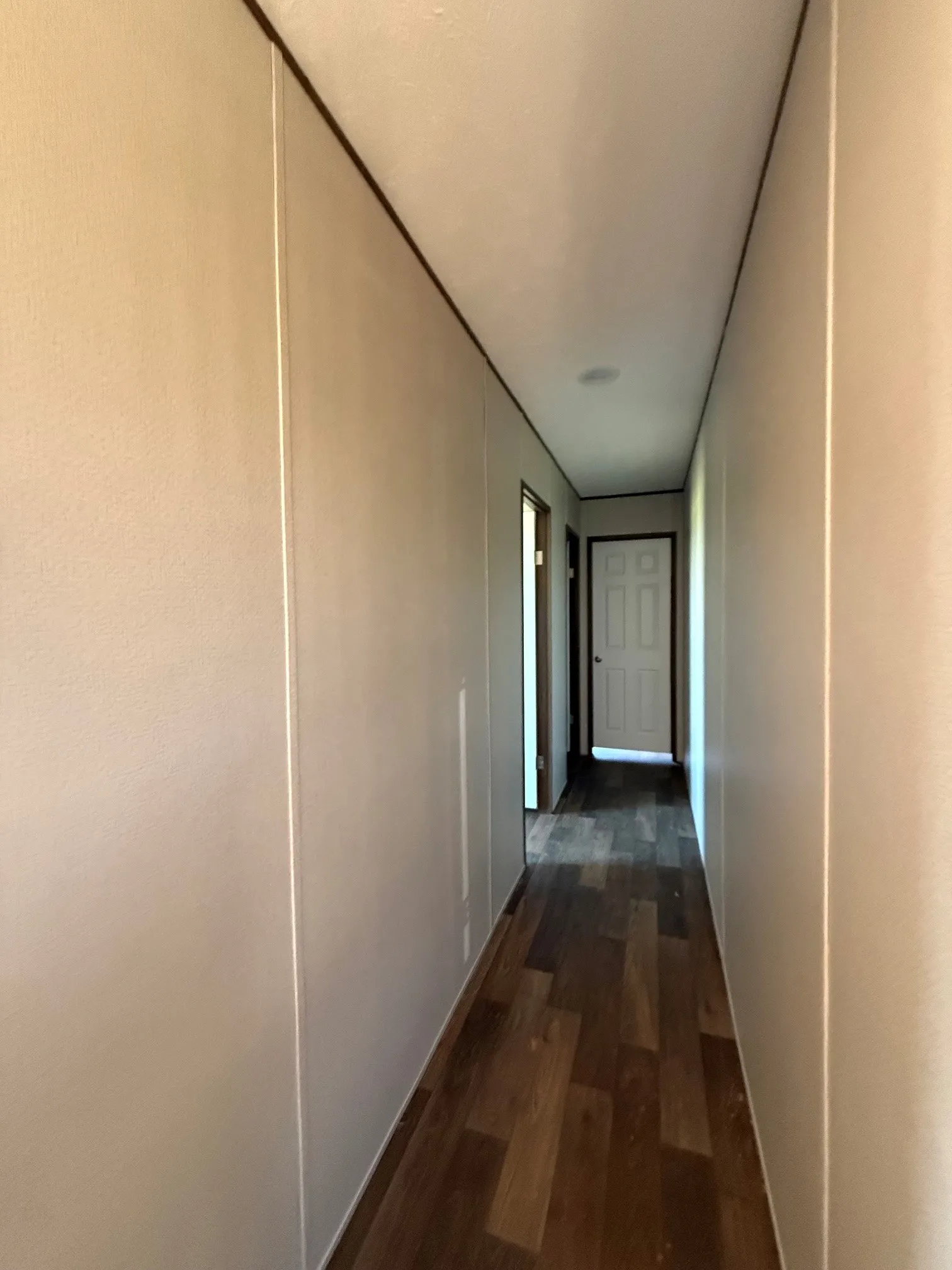 Hallway featuring wood-finish flooring, light-toned walls with vertical paneling, and a white paneled door