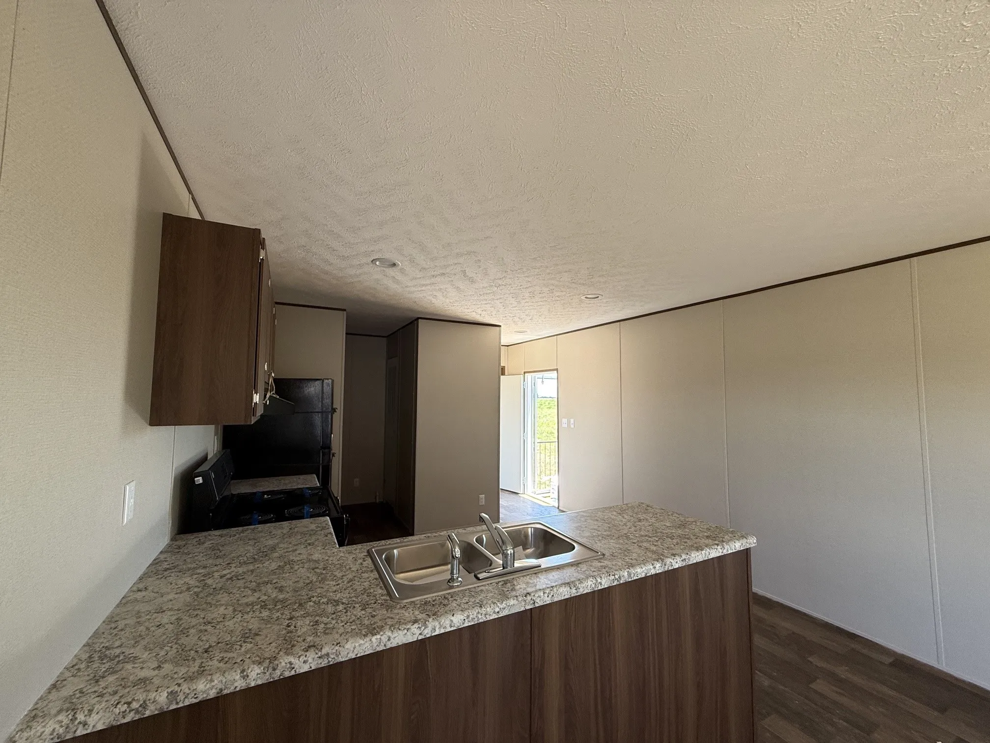 Kitchen area with wood-finish base cabinetry, speckled countertop, and a stainless steel double basin sink