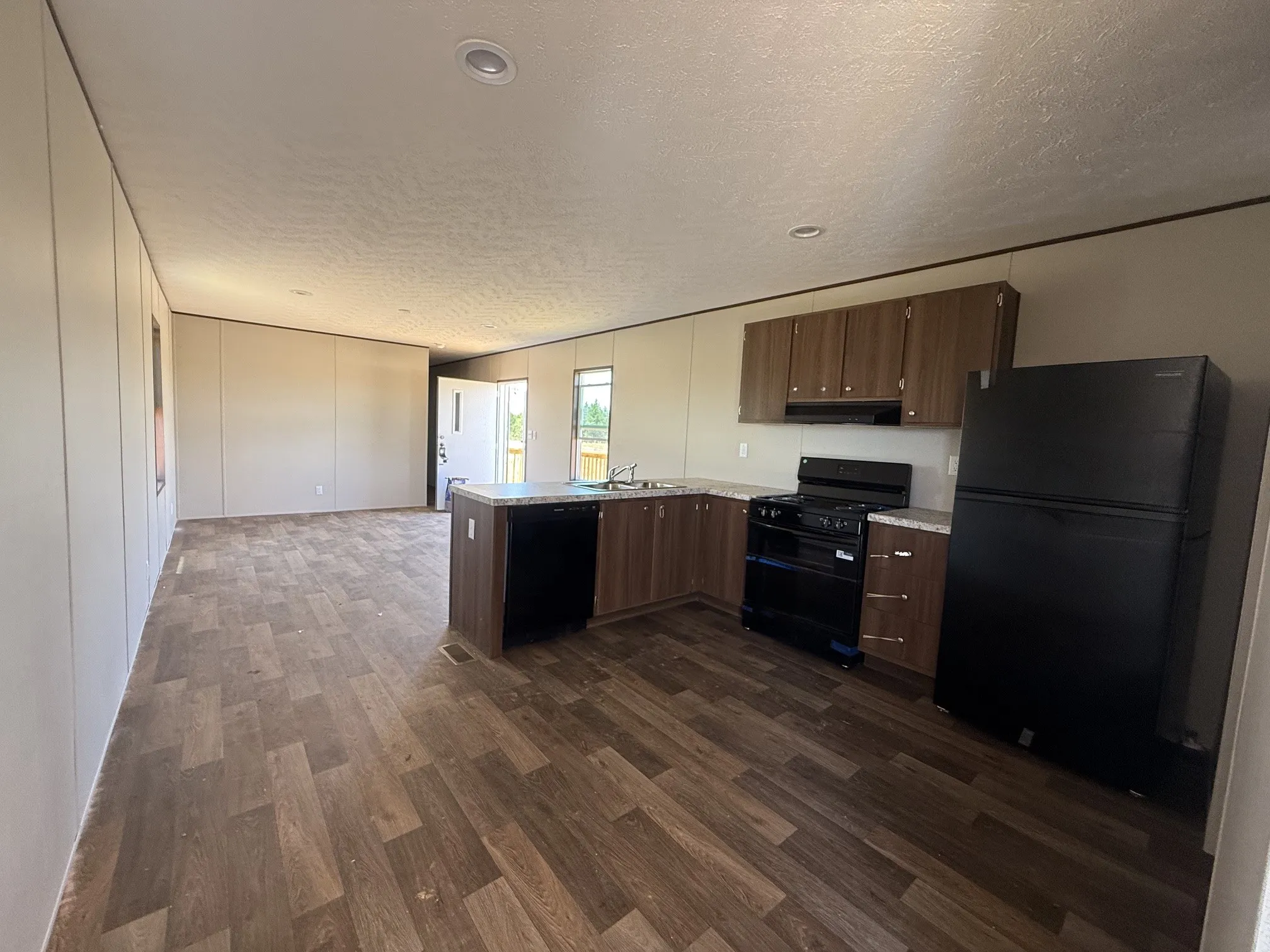 Open-concept kitchen featuring wood-finish cabinetry, black appliances including a refrigerator, stove, and dishwasher, and light-toned countertops