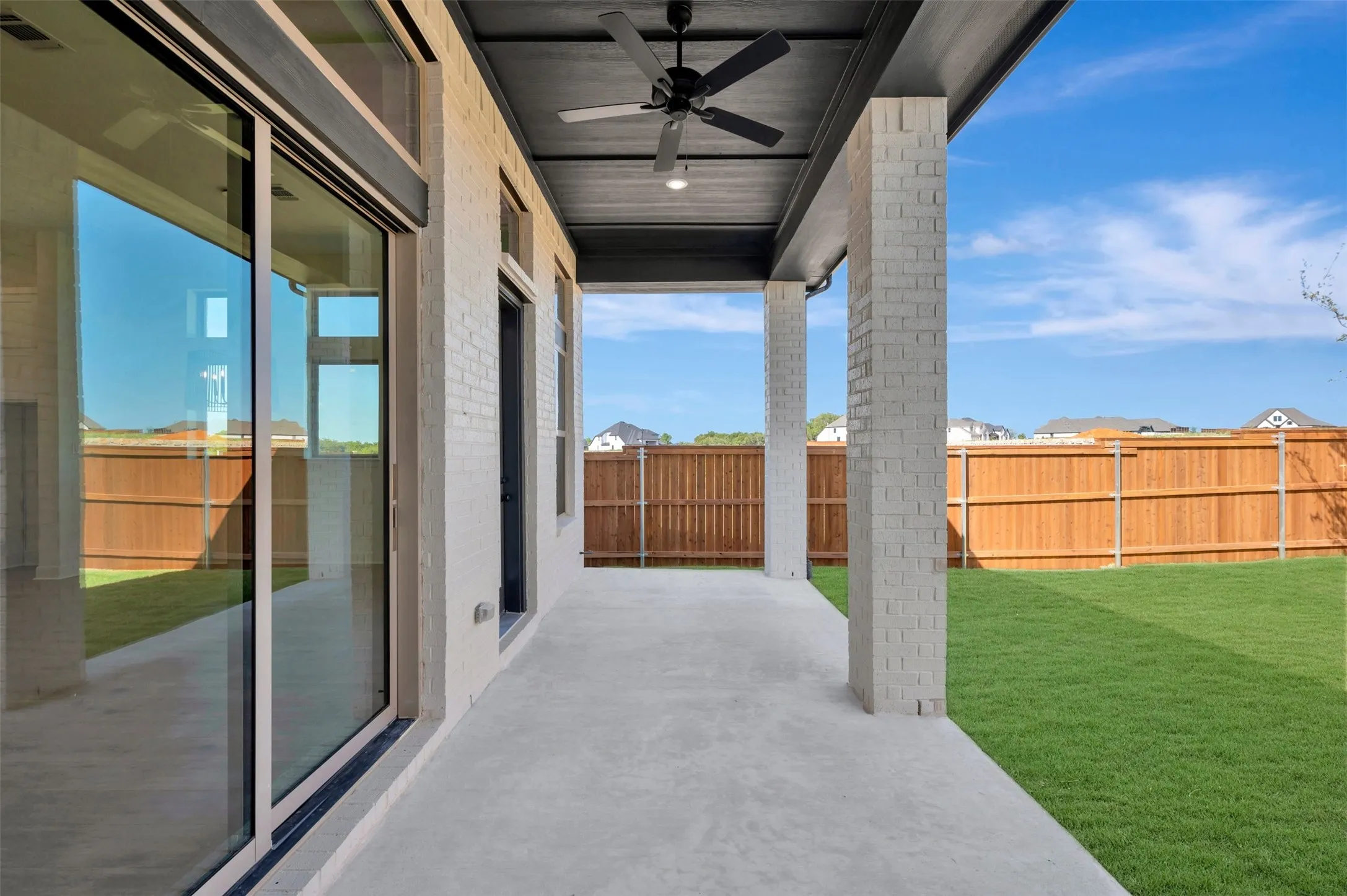 Covered patio featuring a ceiling fan, brick columns, and a concrete surface
