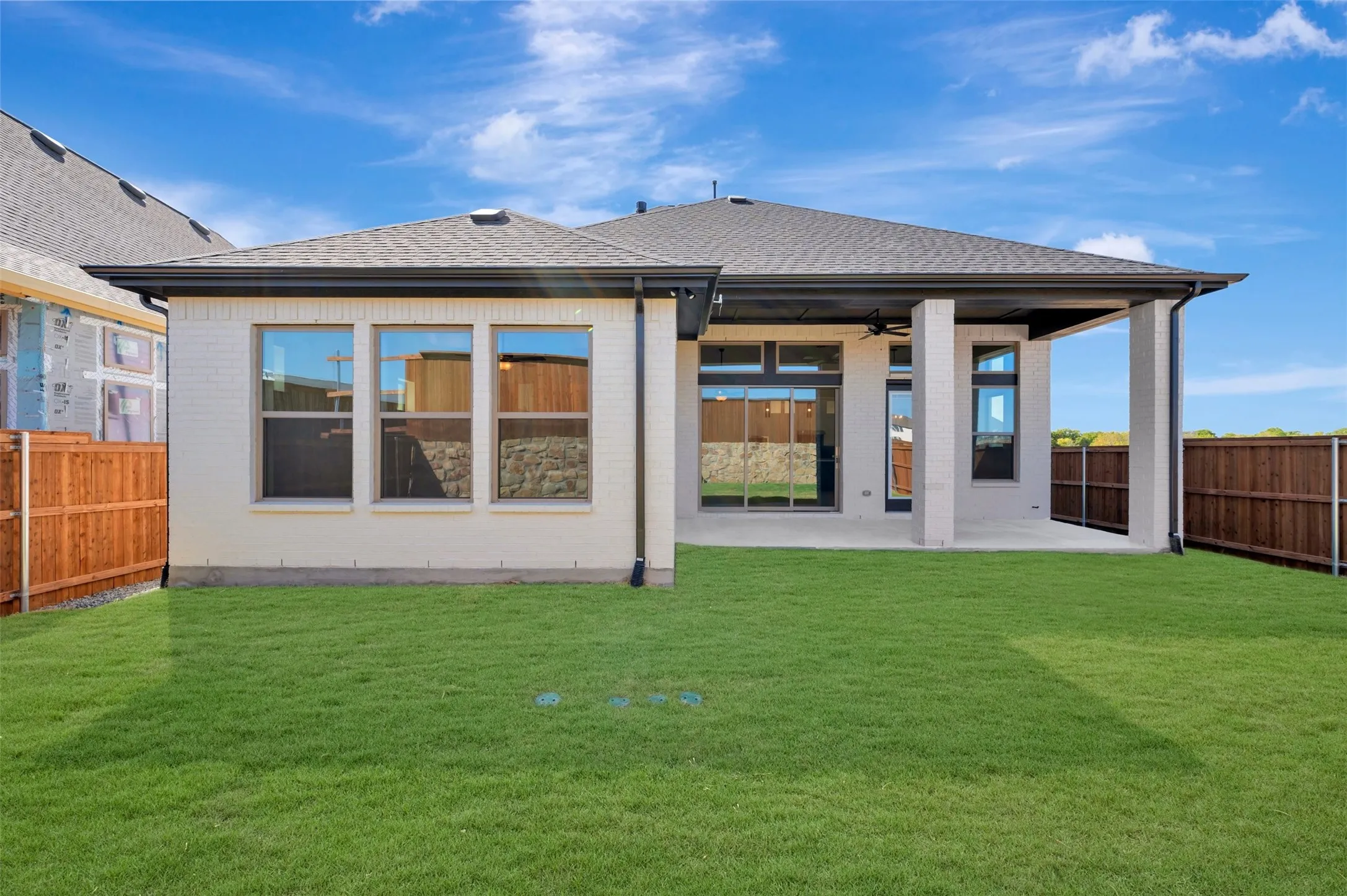 Rear exterior featuring a covered patio, expansive lawn, and privacy fencing