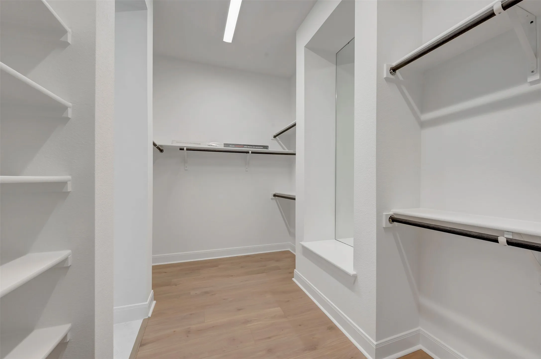 Integrated closet system featuring multiple shelves and hanging rods, light wood-finish flooring, recessed lighting, and a built-in mirror