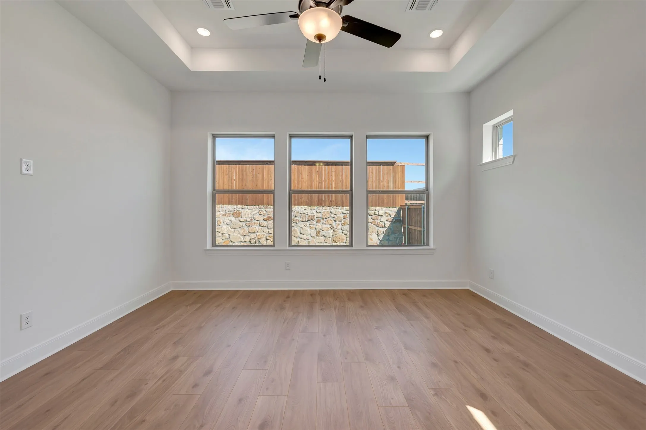 Recessed lighting, ceiling fan, tray ceiling, wood-finish flooring, and multiple windows
