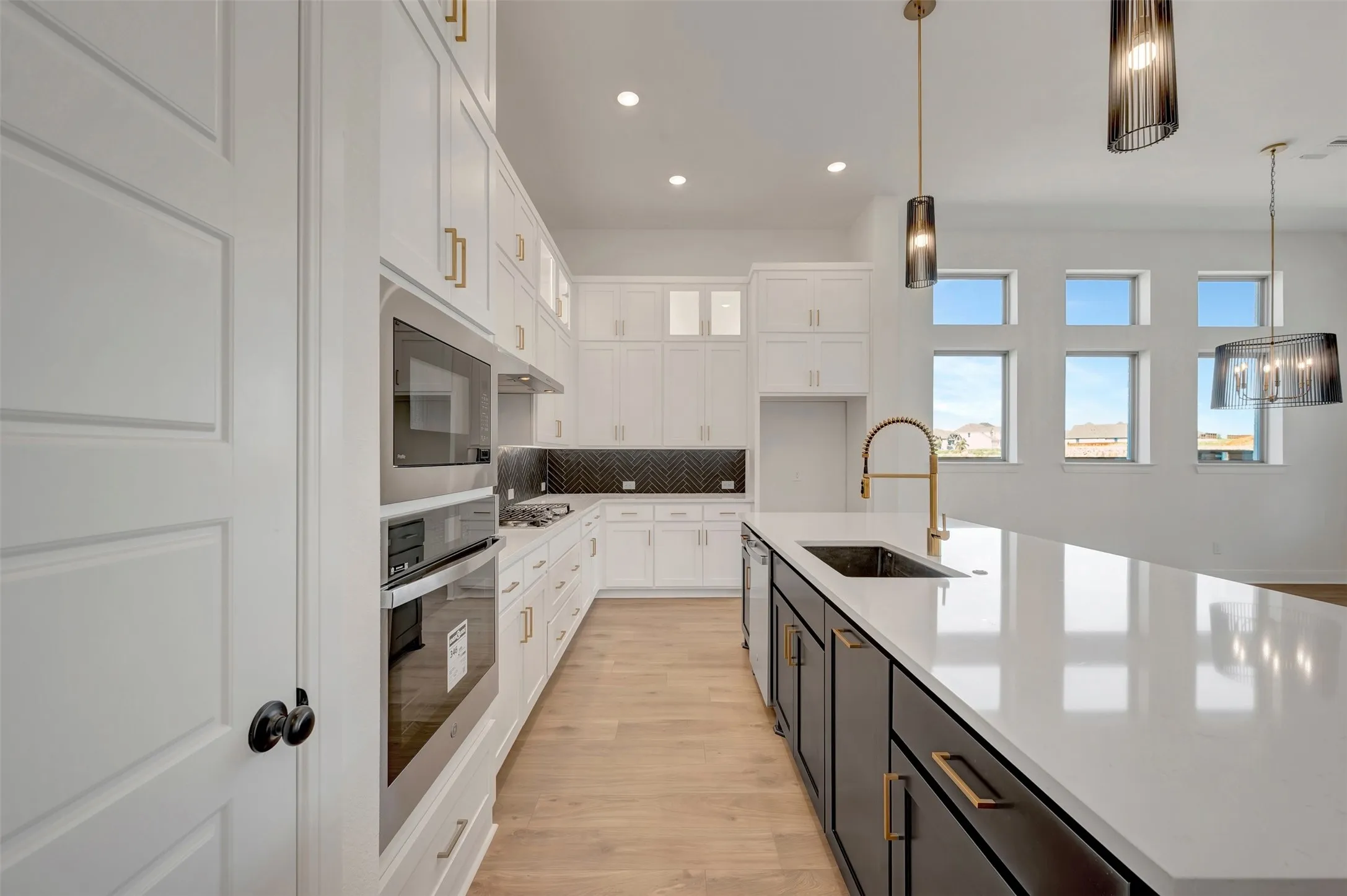 Gourmet kitchen with white cabinetry, stainless steel built-in appliances, a large center island with a sink, and pendant lighting