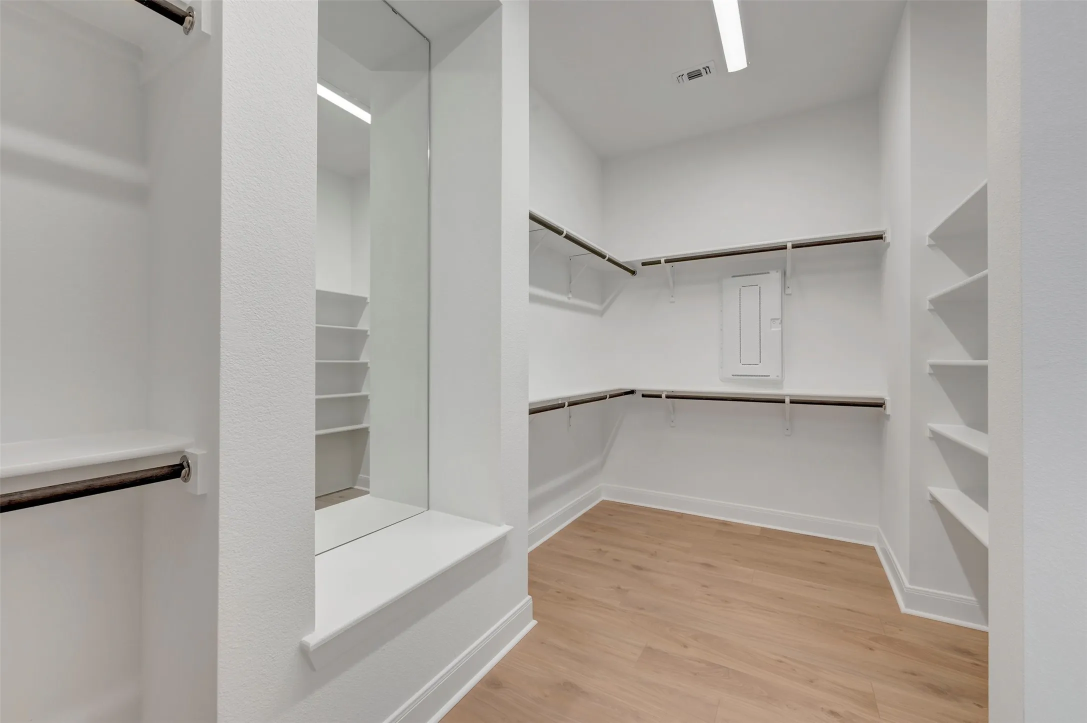 Spacious walk-in closet featuring wood-finish flooring, extensive built-in shelving, multiple hanging rods, a full-length mirrored alcove, and recessed lighting