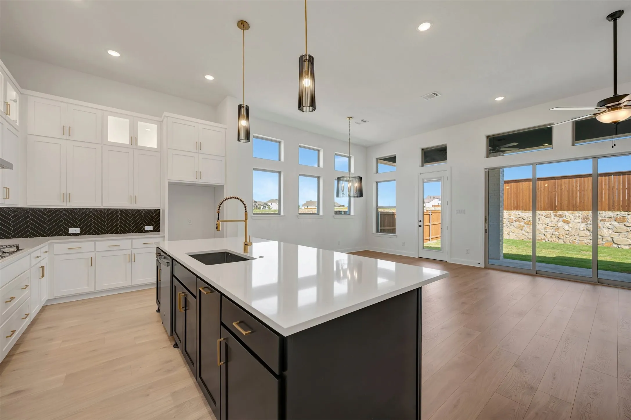 Wood-finish flooring throughout, white upper cabinetry, dark lower cabinetry, white kitchen island with undermount sink, black herringbone tile backsplash, and sliding glass door to the exterior