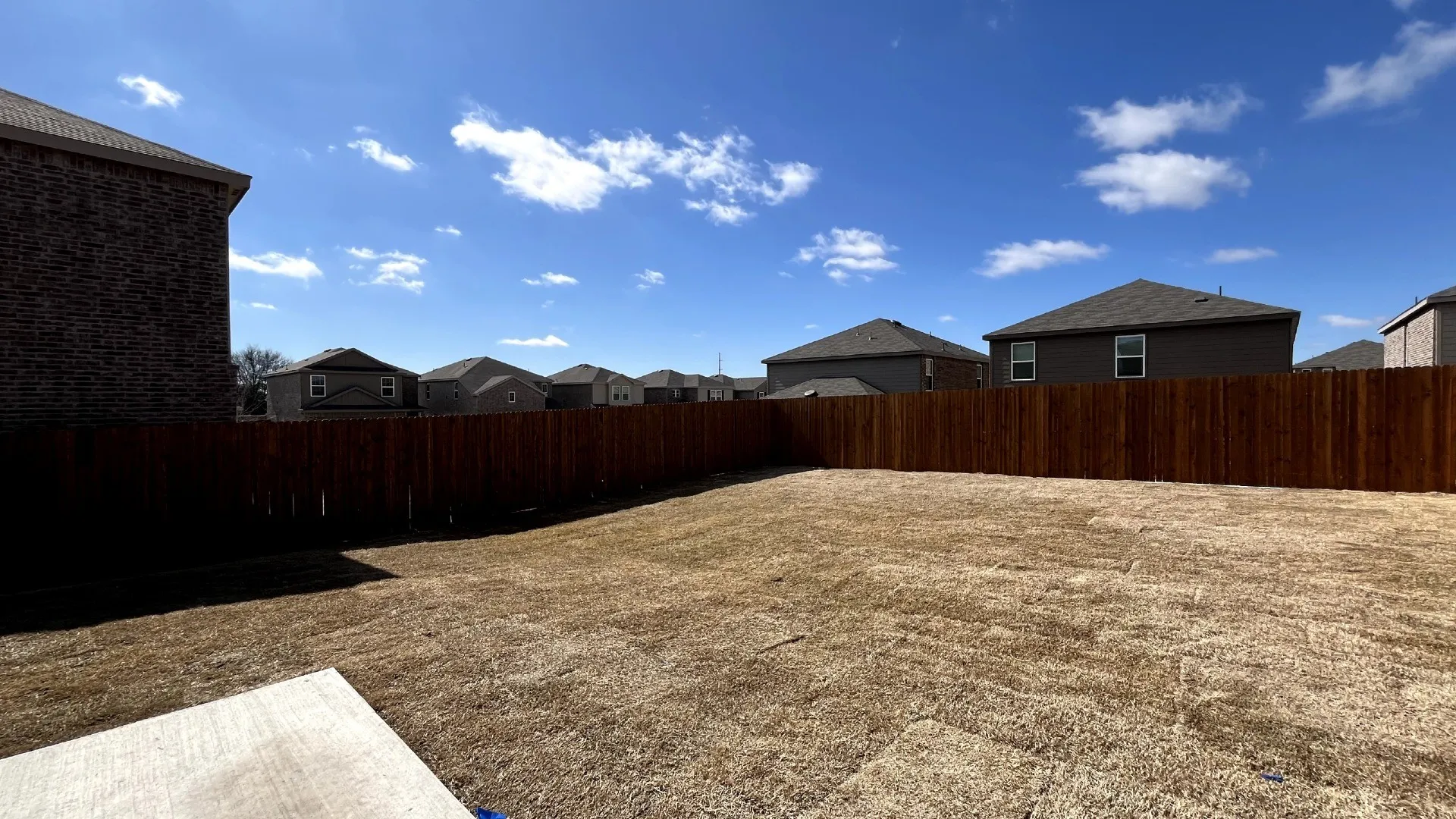 Expansive backyard space featuring a wood privacy fence, a concrete patio area, and a brick exterior wall