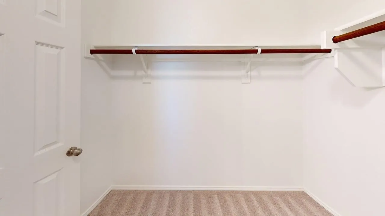 Carpeted closet space featuring white walls and baseboards, a white two-panel door with a brass knob, and wood-finish closet rods with white shelving