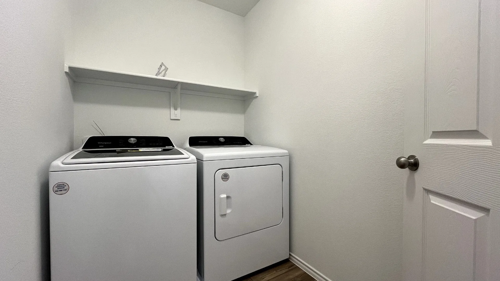 Dedicated utility space featuring a built-in shelf, neutral wall tones, wood-finish flooring, and a paneled door