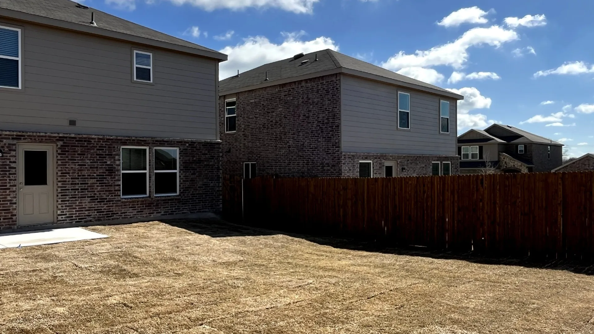 Expansive backyard featuring a new privacy fence, partial brick and siding exterior, multiple windows, and a rear entry door leading to a concrete patio