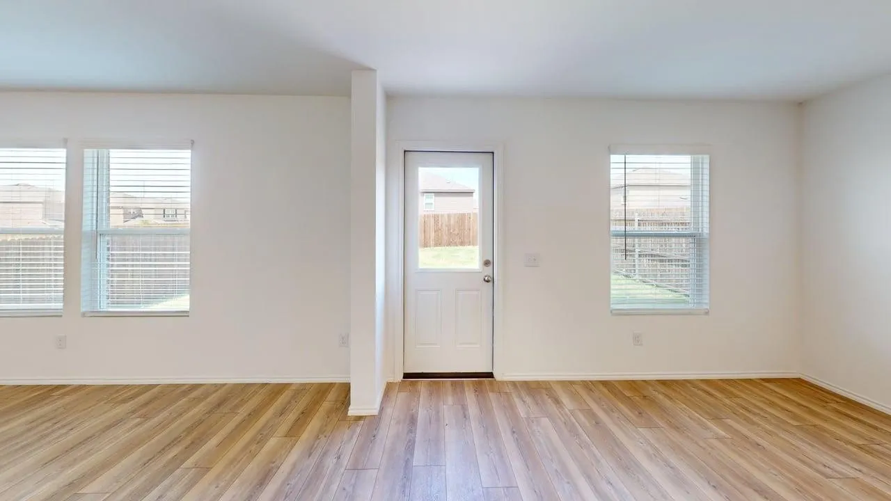 Spacious room featuring wood-finish flooring, white walls, multiple windows with blinds, and a white egress door