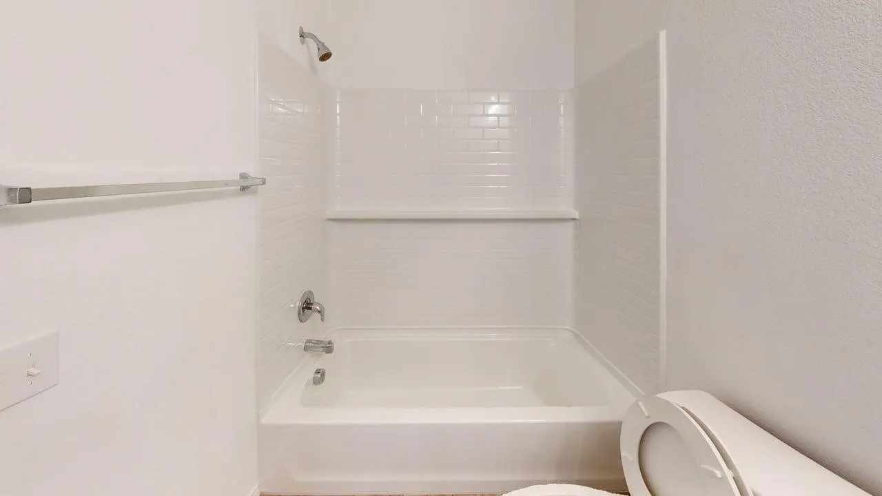 Bathtub with white subway tile surround, integrated shower fixture, and a chrome towel bar