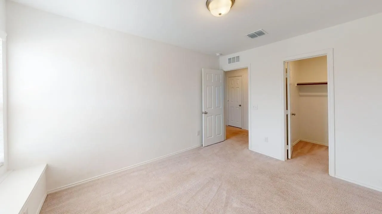 Neutral-toned carpeted interior space featuring a window with a built-in bench, flush mount ceiling light, white paneled doors, and a closet with a built-in shelf and hanging rod
