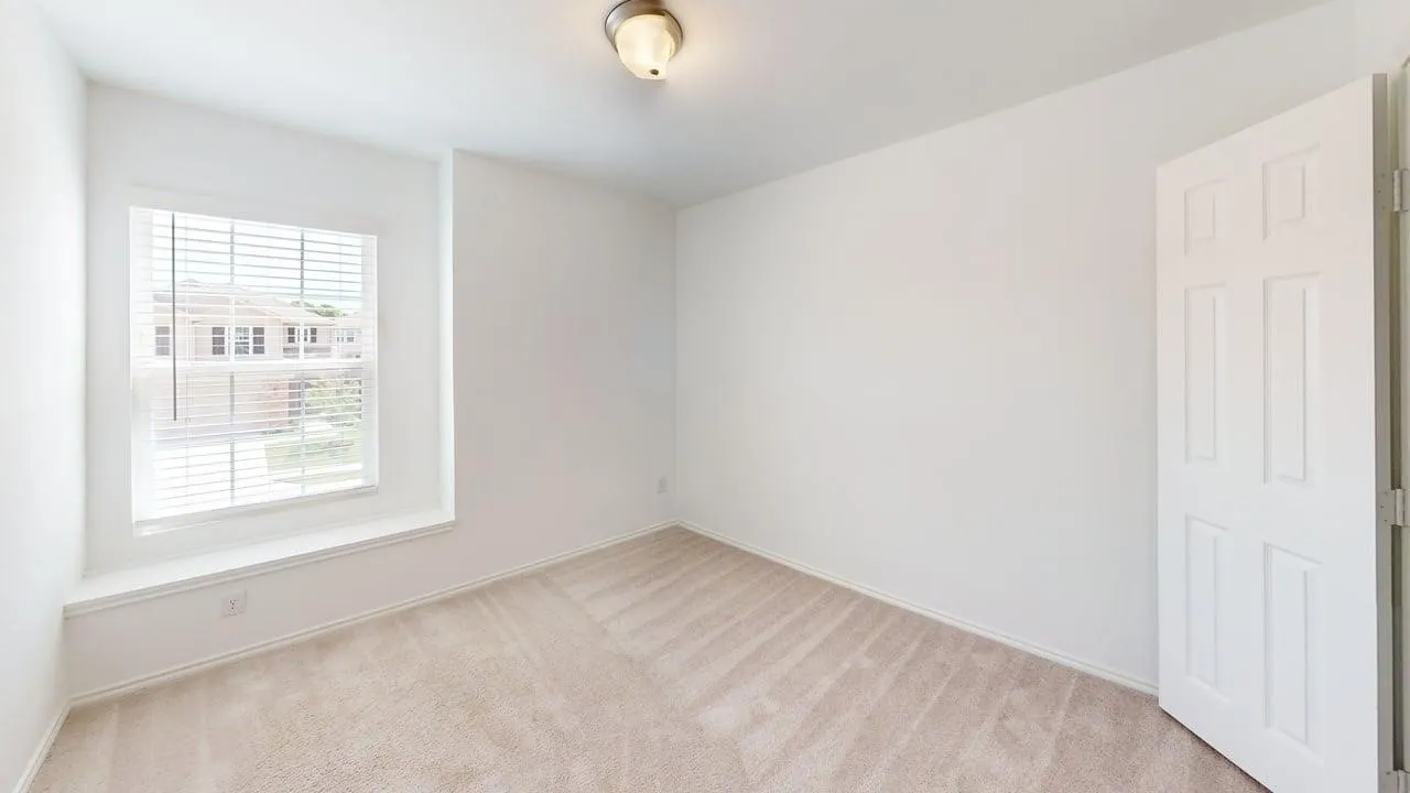 Bedroom featuring neutral carpeting, a large window with white blinds, and a paneled door
