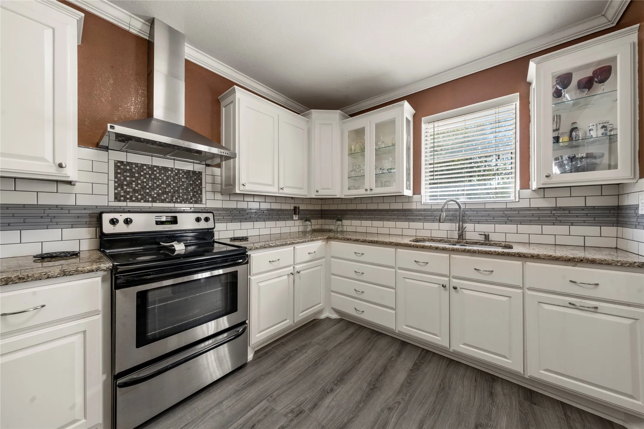 Kitchen featuring white cabinetry, light-toned countertops, a stainless steel range with a coordinating vent hood, and wood-finish flooring