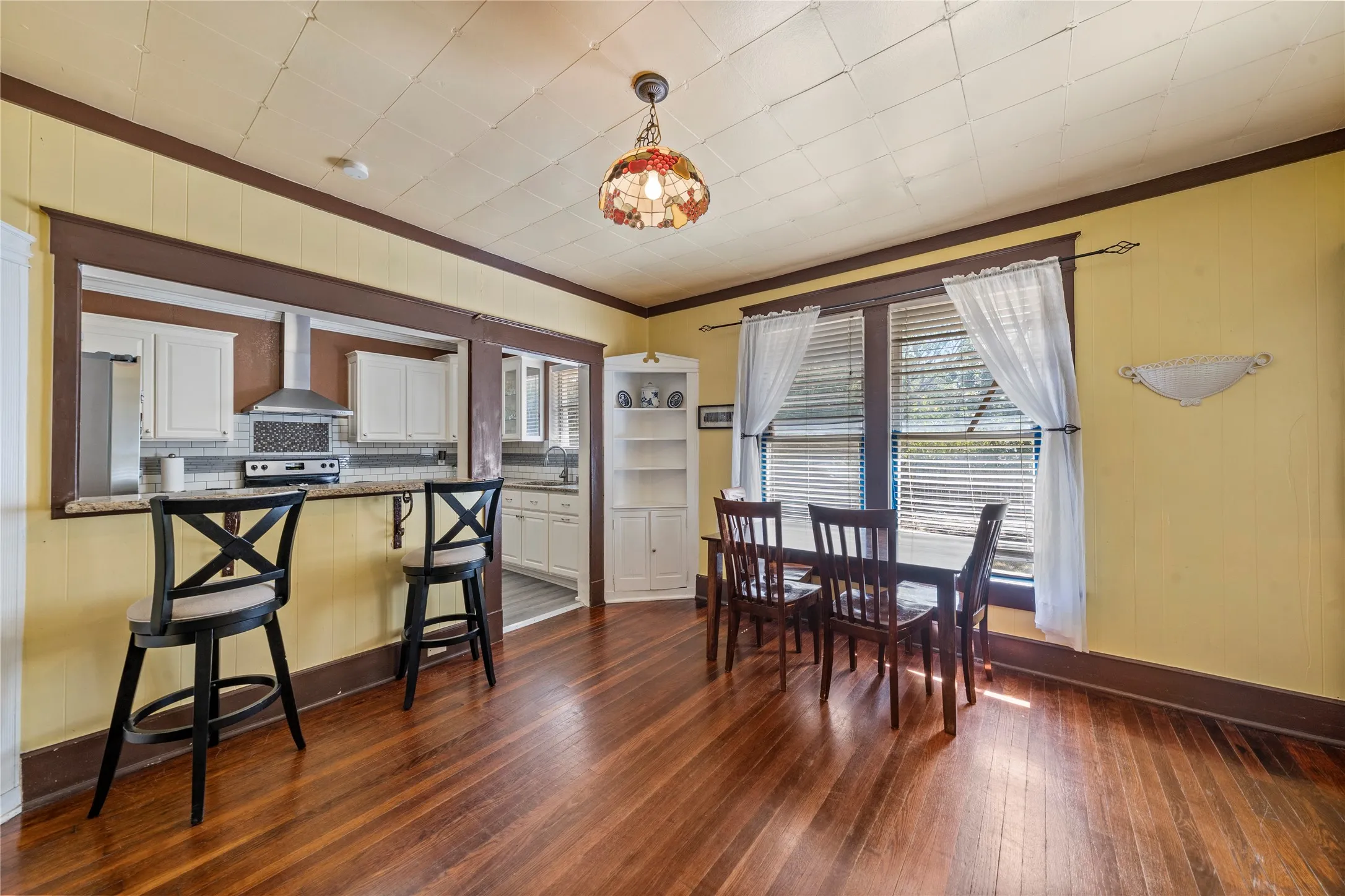 Hardwood flooring throughout, a pass-through kitchen with white cabinetry and stainless steel appliances, a corner built-in shelving unit, and multiple windows
