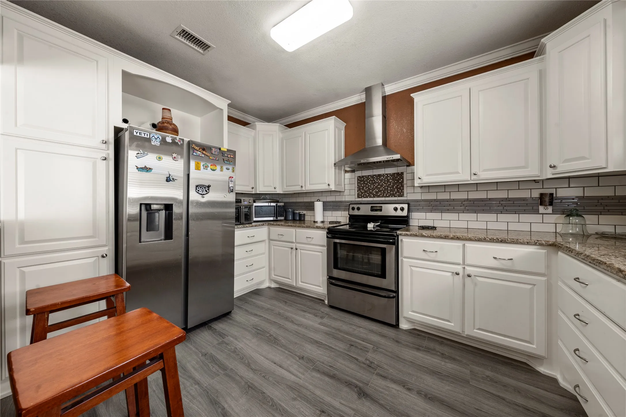White cabinetry, stainless steel appliances, granite countertops, wood-finish flooring, and subway tile backsplash
