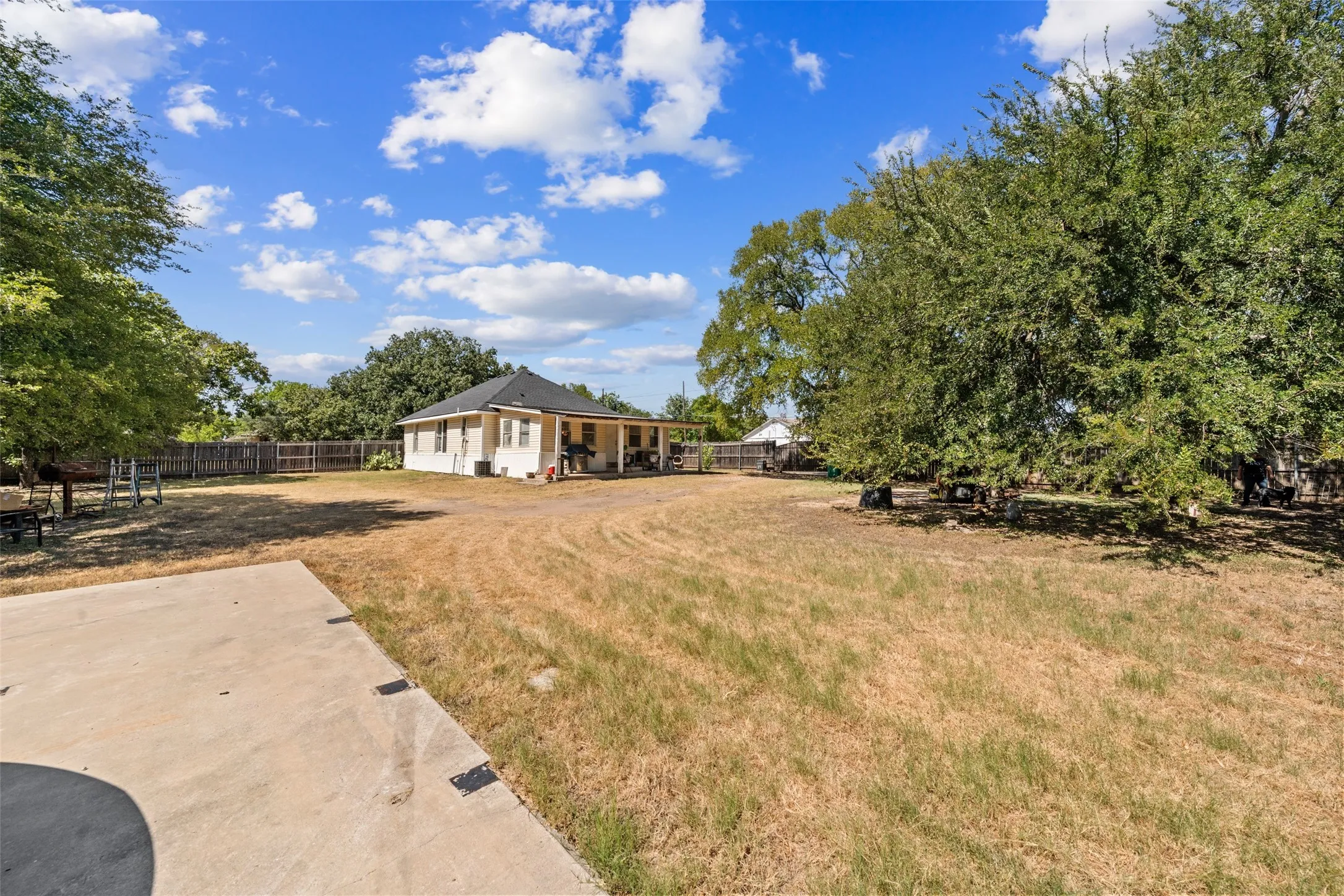 Expansive backyard featuring mature trees, a concrete patio, and a wood privacy fence