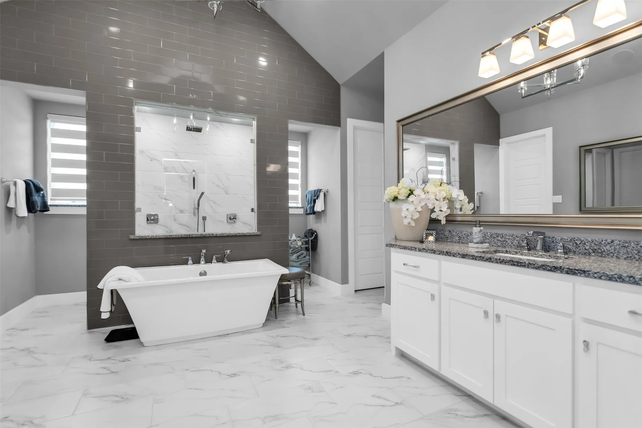 Spacious bathroom featuring a freestanding tub, expansive walk-in shower with glass enclosure, dual vanity with undermount sinks and stone countertop, large wall-mounted mirror, and tile flooring