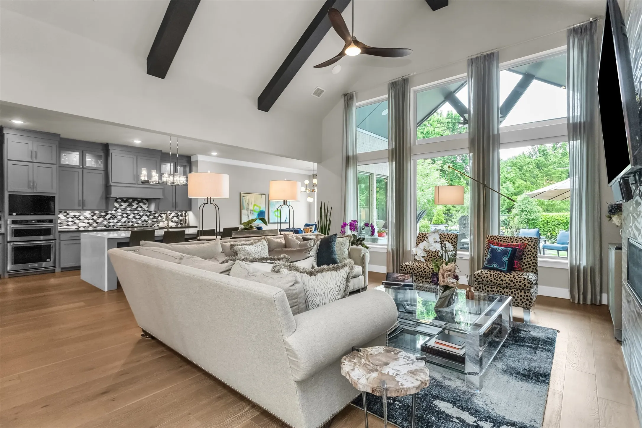 Open-concept living area featuring a vaulted ceiling with exposed beams, wood-finish flooring, and a wall of tall windows