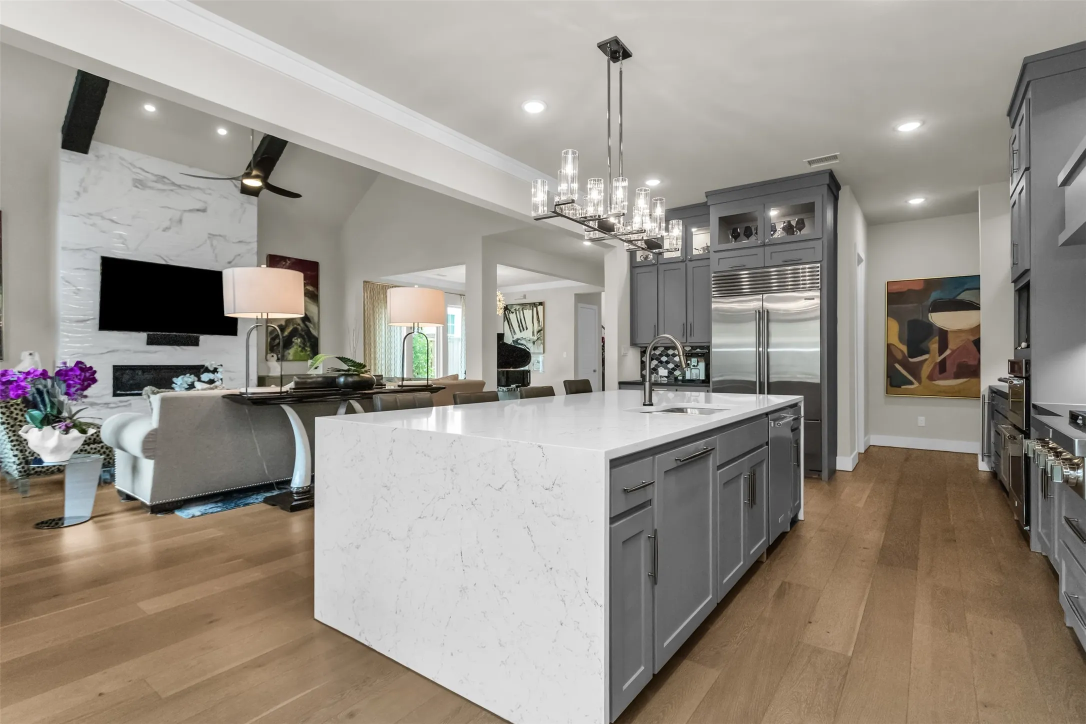 Gourmet kitchen with a large central island, light-toned wood-finish flooring, and integrated stainless steel appliances