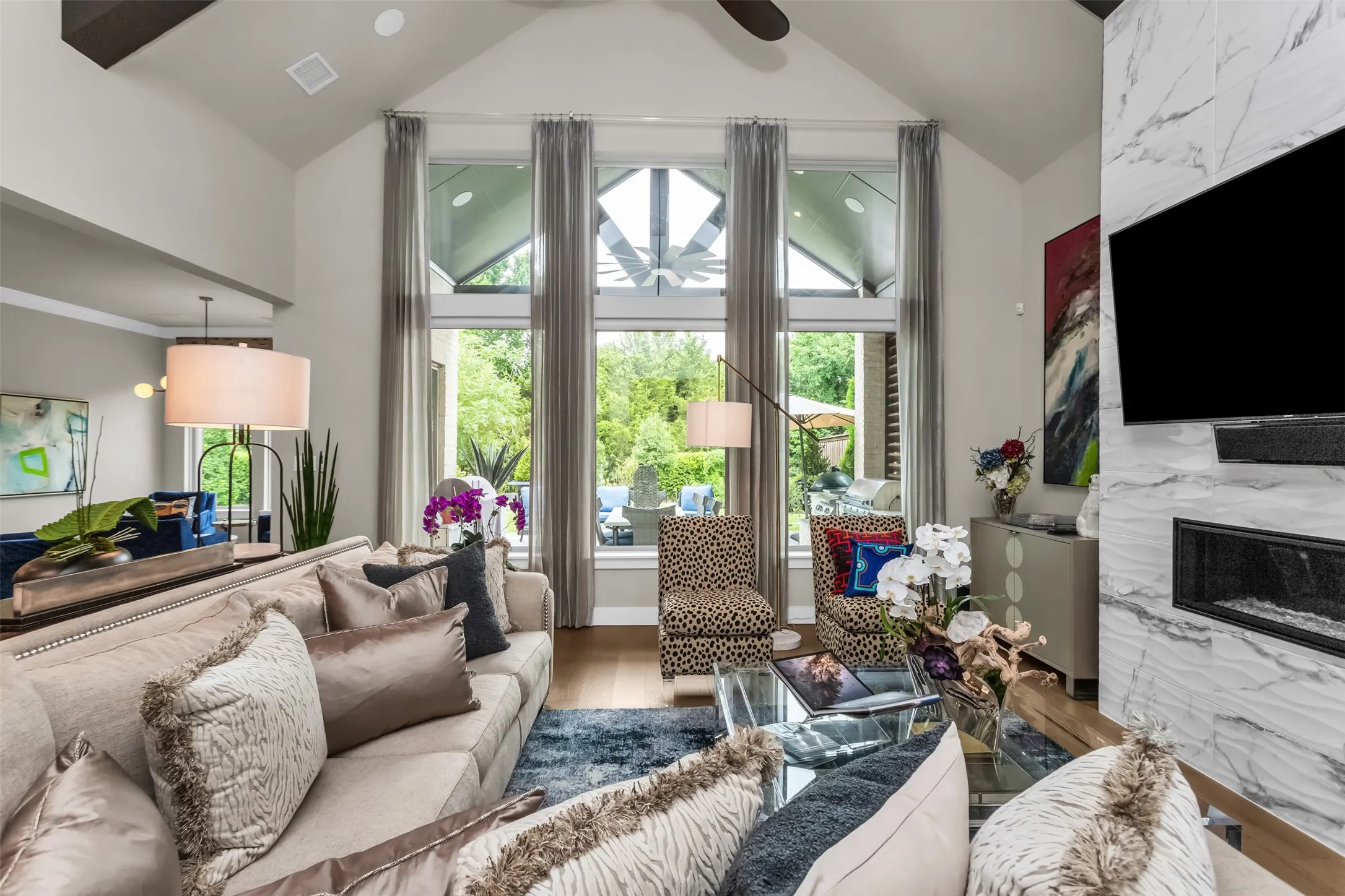 Vaulted ceiling living area featuring a linear gas fireplace with a marble-finish surround, wood-finish flooring, and expansive windows