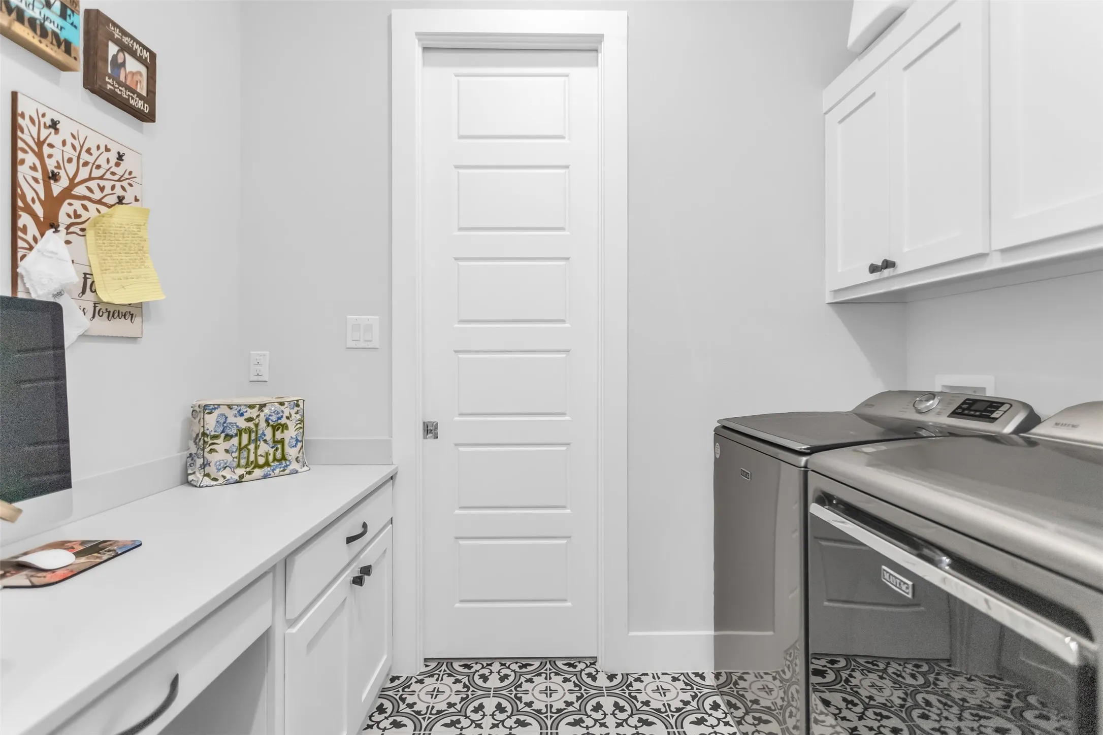 Laundry area featuring patterned floor tile, white shaker-style cabinetry, a built-in countertop with an integrated desk space, and a five-panel interior door