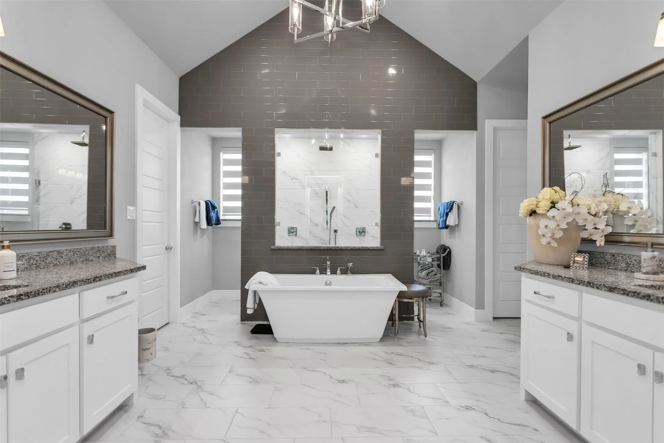 Freestanding soaking tub with dual showers, set against a dark gray subway tile accent wall and white marble-look flooring
