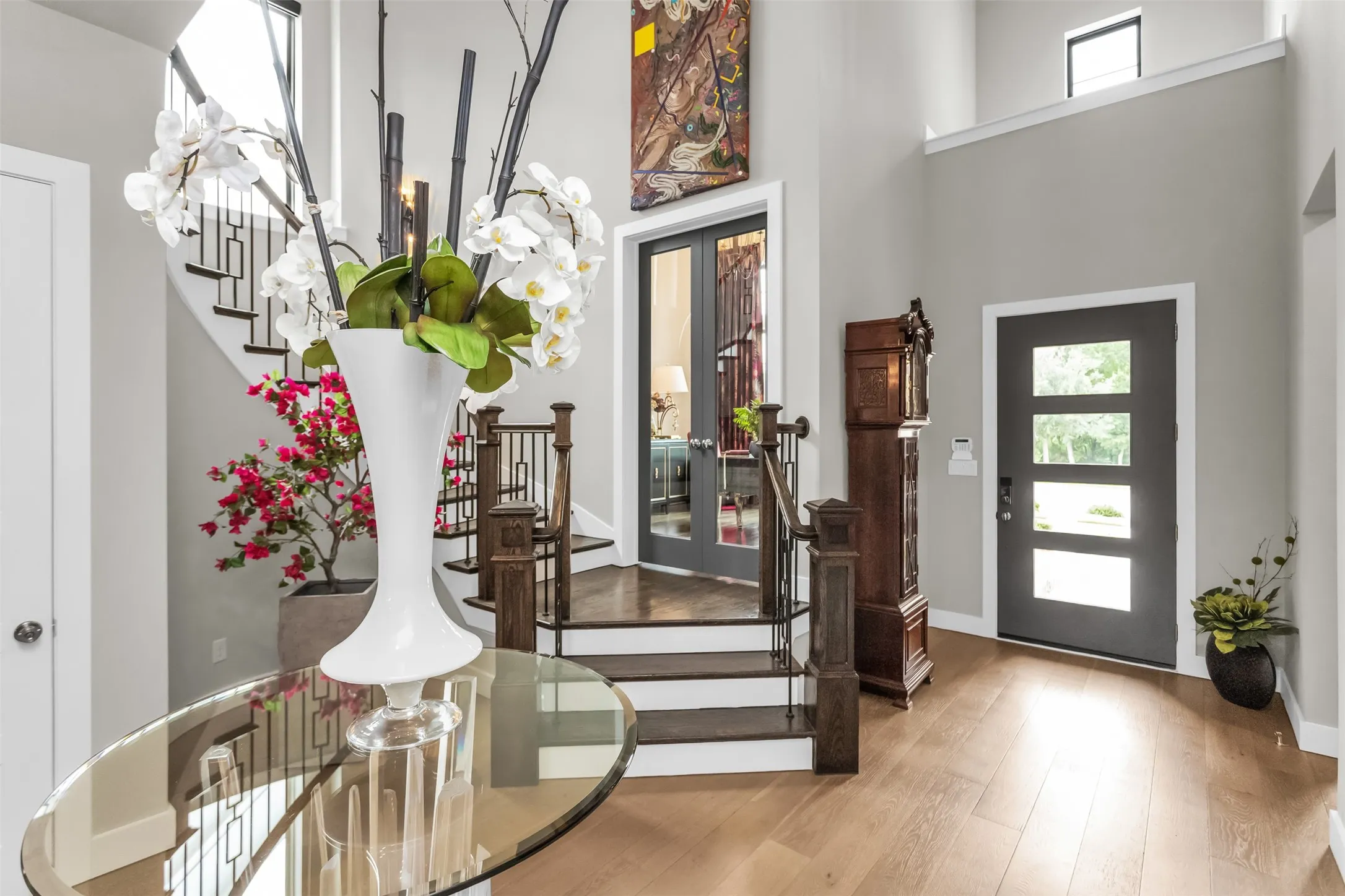 Grand foyer with high ceilings, light wood-finish flooring, a contemporary staircase featuring dark wood treads and wrought iron railings, and a multi-paneled entry door