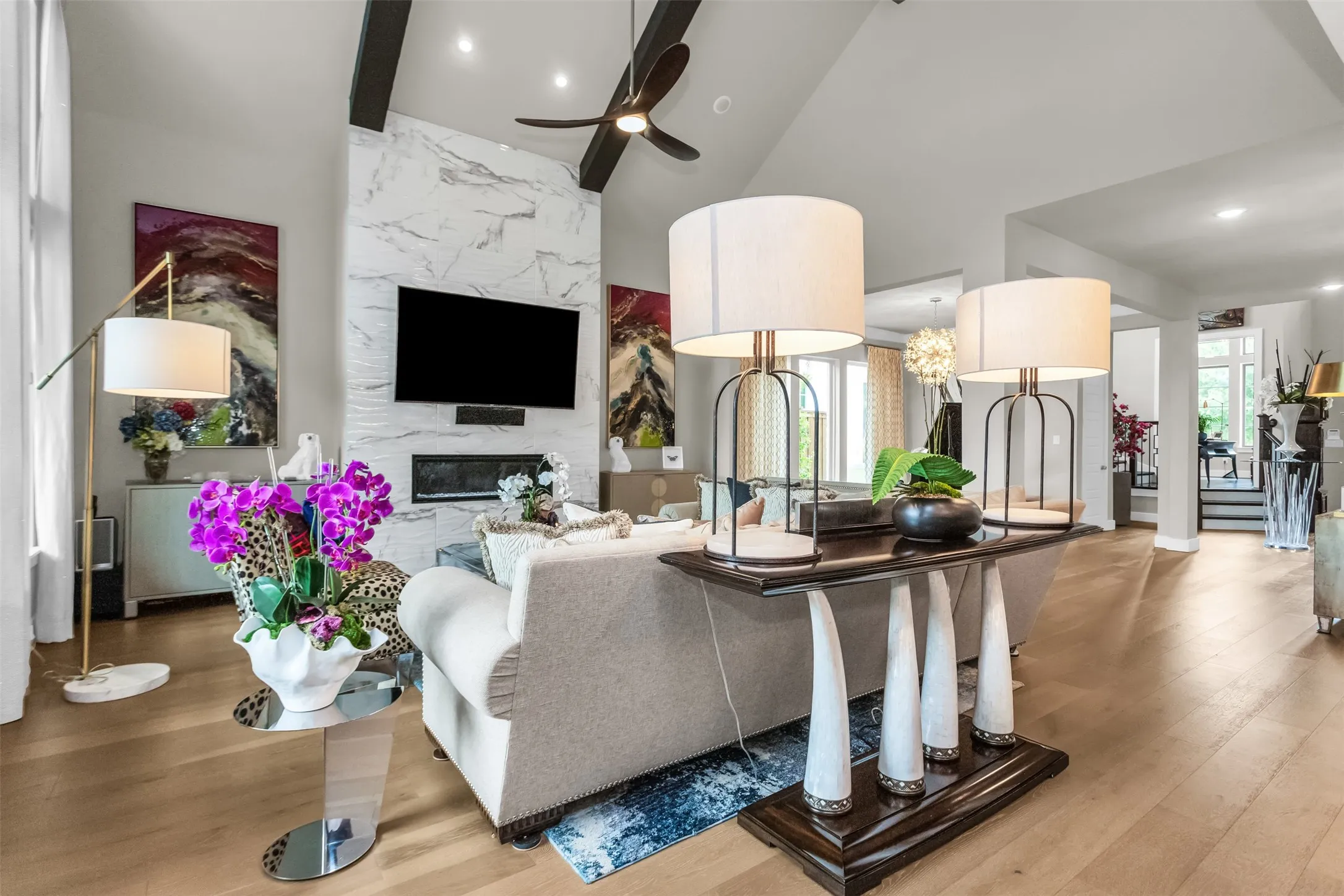 Vaulted ceiling living space featuring a floor-to-ceiling fireplace with an integrated television, exposed ceiling beams, a ceiling fan, and wood-finish flooring
