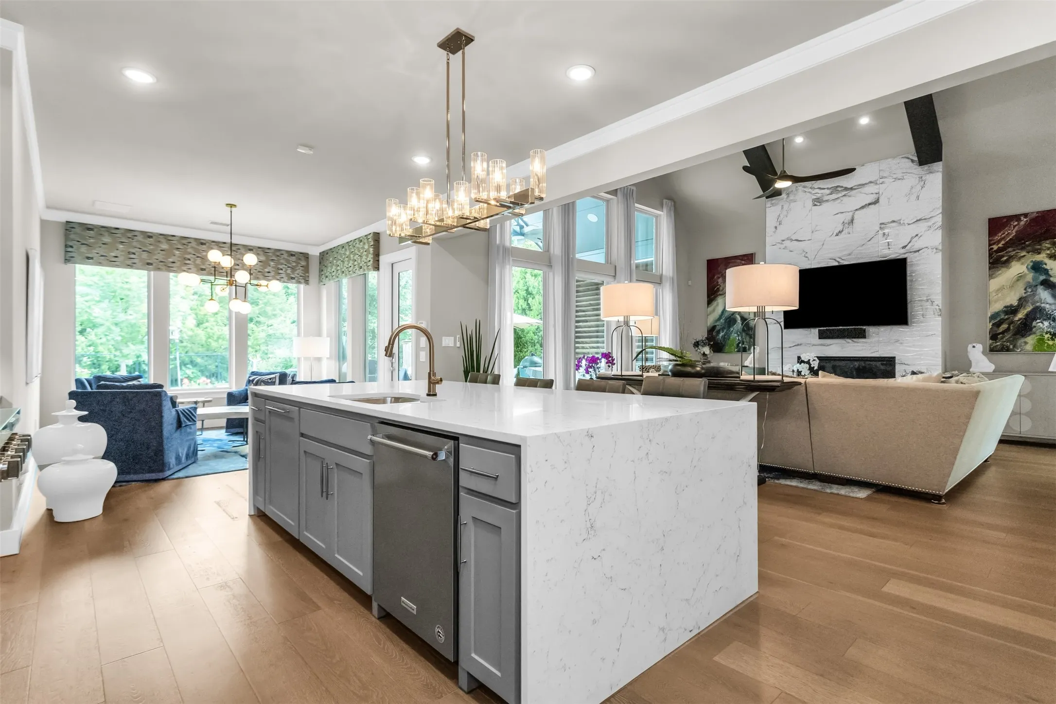 Expansive kitchen island with a waterfall countertop, integrated sink, and stainless steel dishwasher