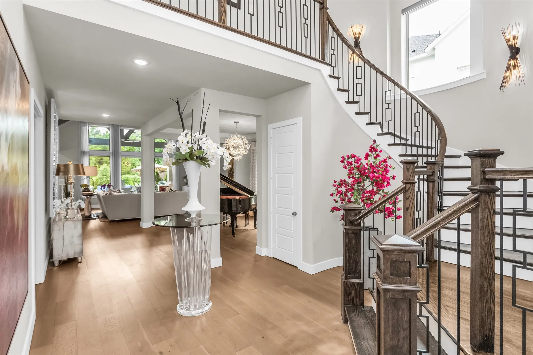 Gracious entry foyer featuring light wood-finish flooring, a grand curved staircase with dark wood newel posts and iron balusters, and elegant wall sconces