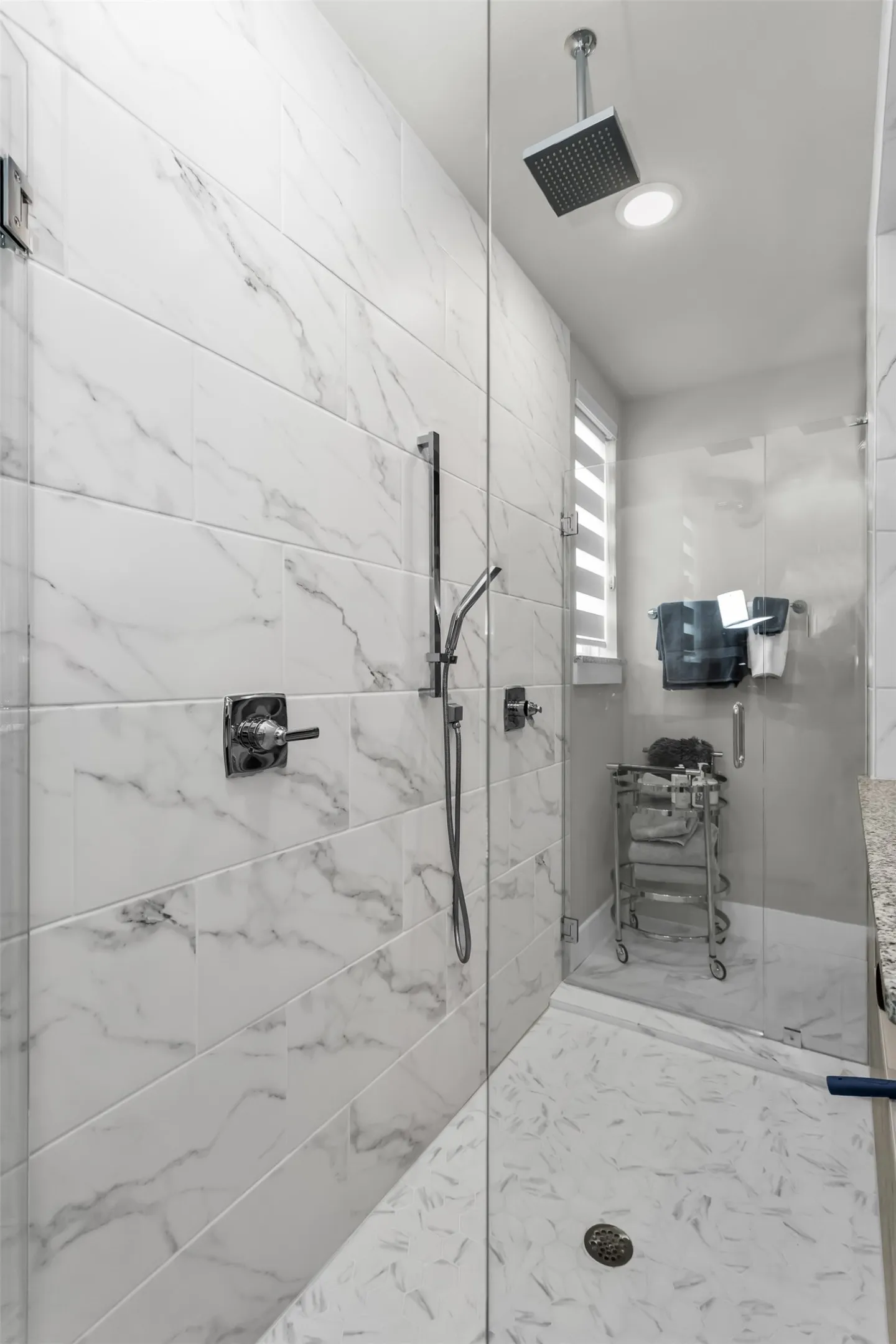 Glass-enclosed shower featuring large format wall tiles, a rain showerhead, a handheld shower fixture, and a mosaic tiled floor