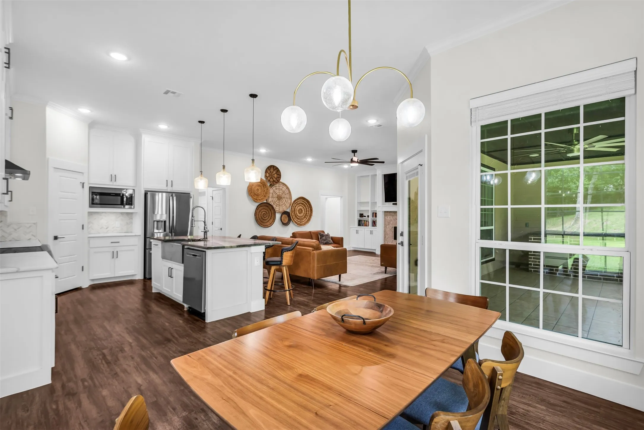 Open-concept kitchen and dining area featuring wood-finish flooring, white cabinetry, a kitchen island with a farmhouse sink, stainless steel appliances, and a dining area with a contemporary chandelier
