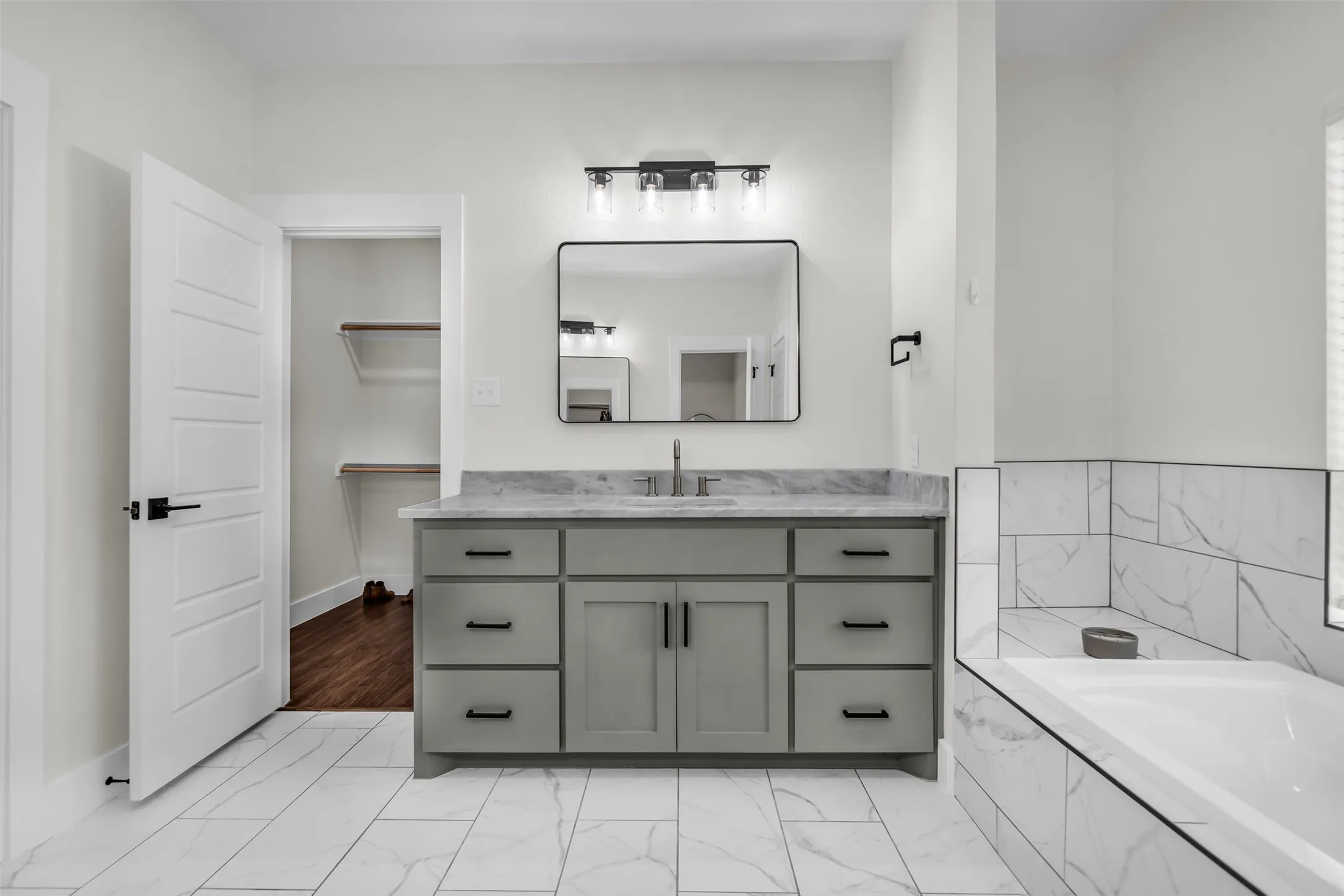 Vanity with gray cabinetry and gray-veined countertop, framed mirror, and contemporary light fixture