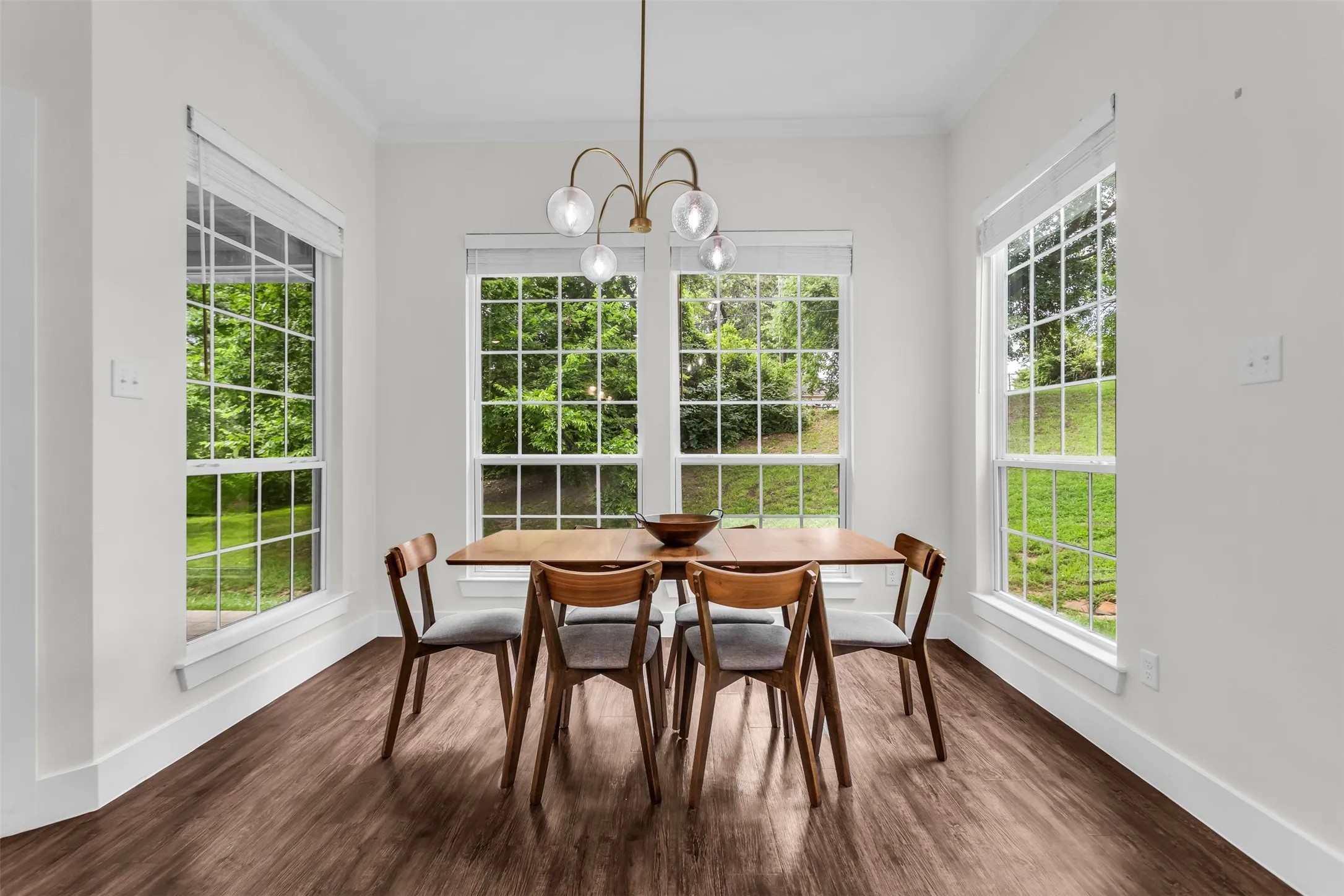 Dining area featuring four large windows with muntin bars, wood-finish flooring, and crown molding
