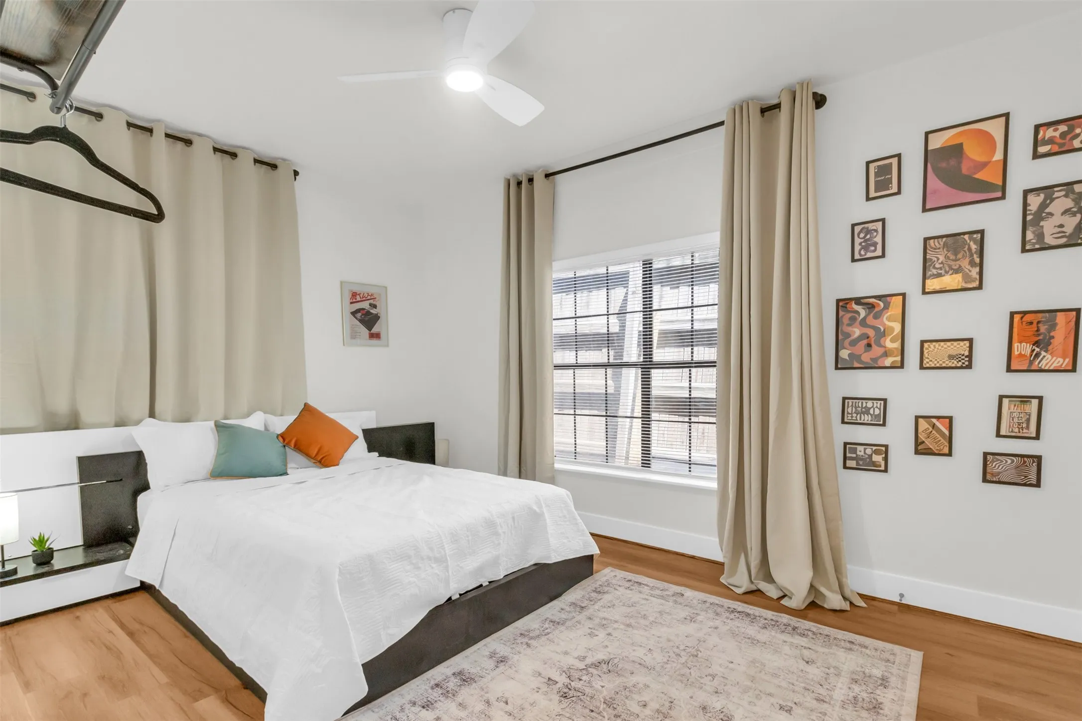 Bedroom featuring wood-finish flooring, a ceiling fan, and a large window with blinds