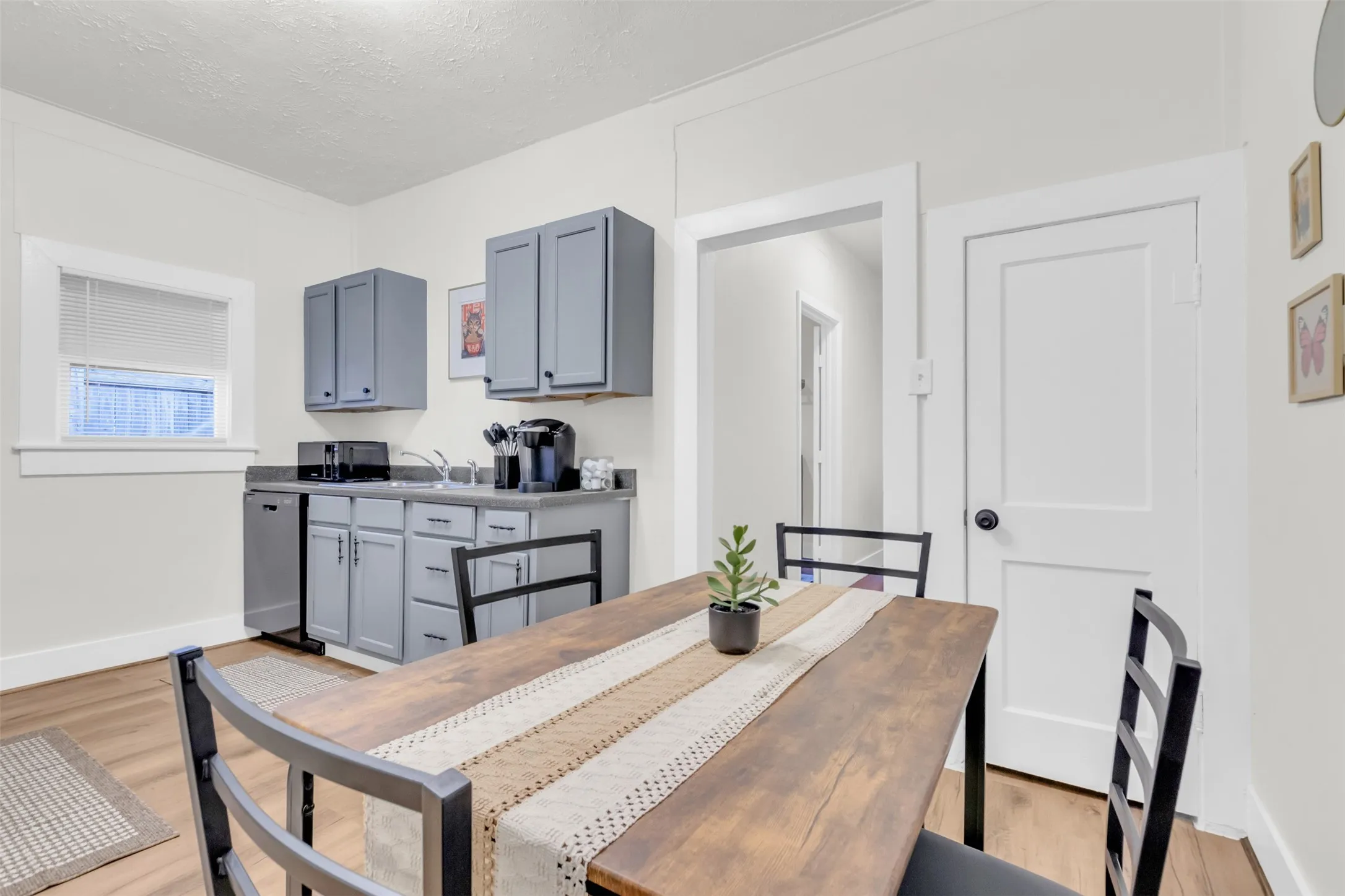 Compact kitchen featuring gray cabinetry, a stainless steel dishwasher, a single basin sink, and wood-finish flooring