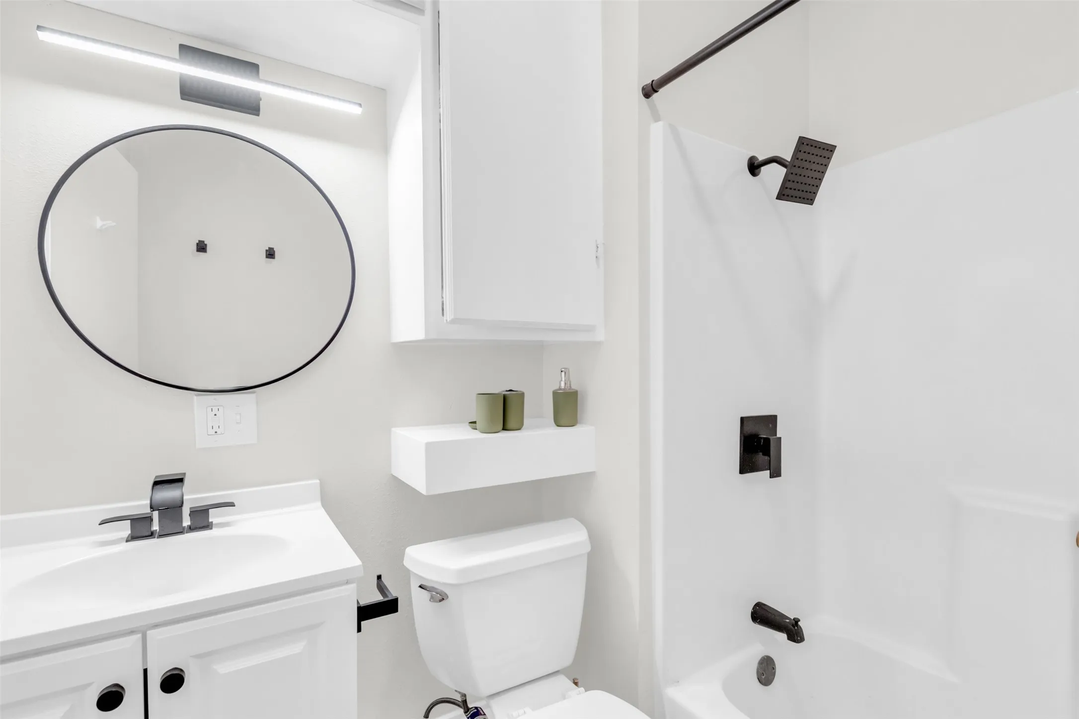 Contemporary bathroom featuring a white vanity with integrated sink, matte black fixtures, an oval mirror, and a shower-over-tub combination with a rainfall showerhead