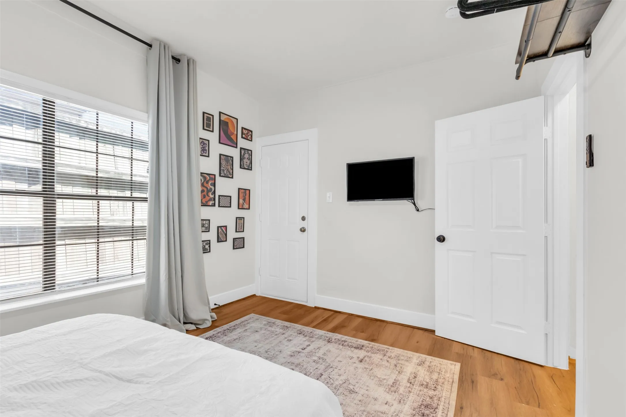 Bright interior space featuring wood-finish flooring, white baseboards, and a large window with horizontal blinds and drapery