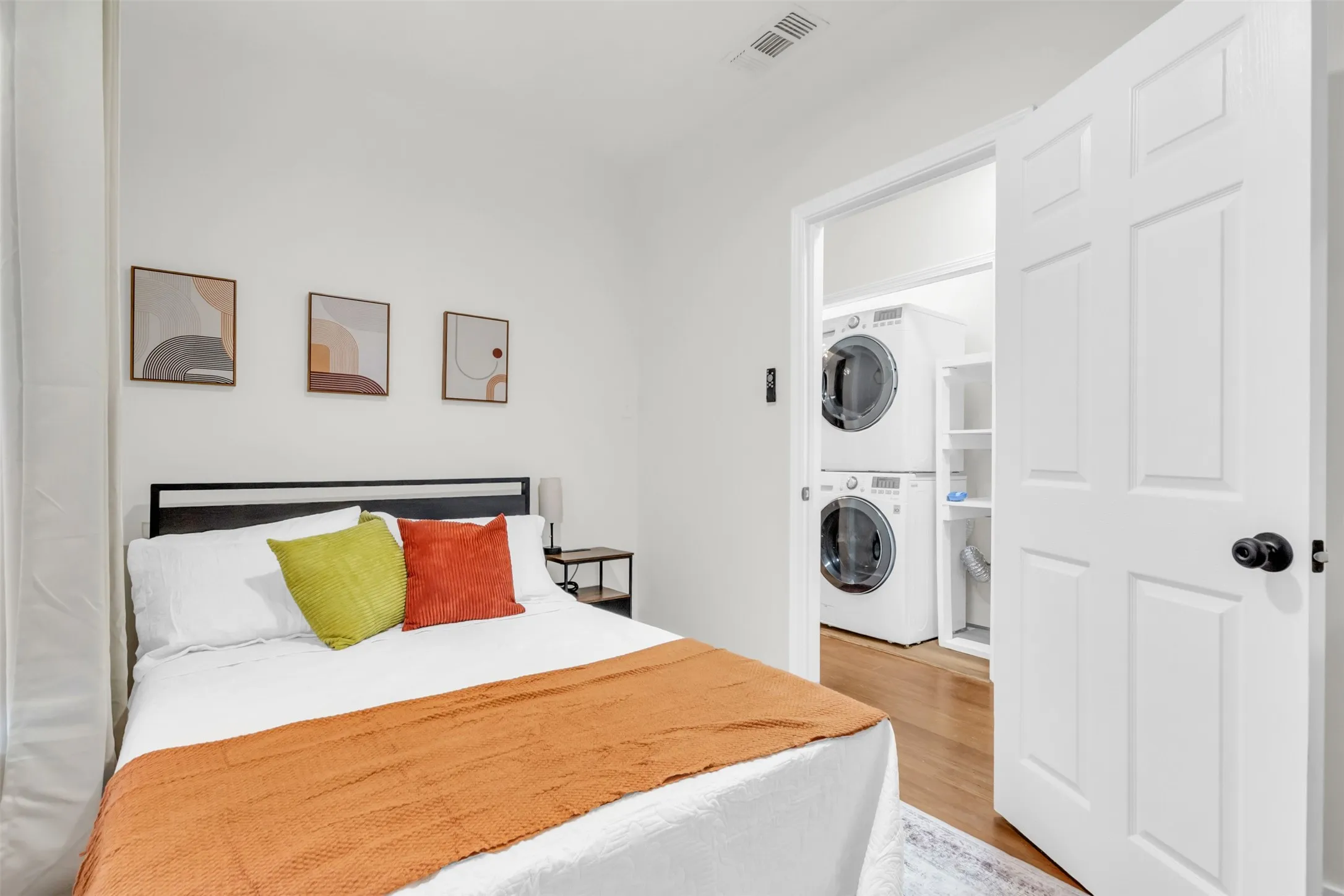 Bedroom featuring a stacked washer and dryer in a dedicated closet, hardwood-style flooring, white walls, and a recessed ceiling vent