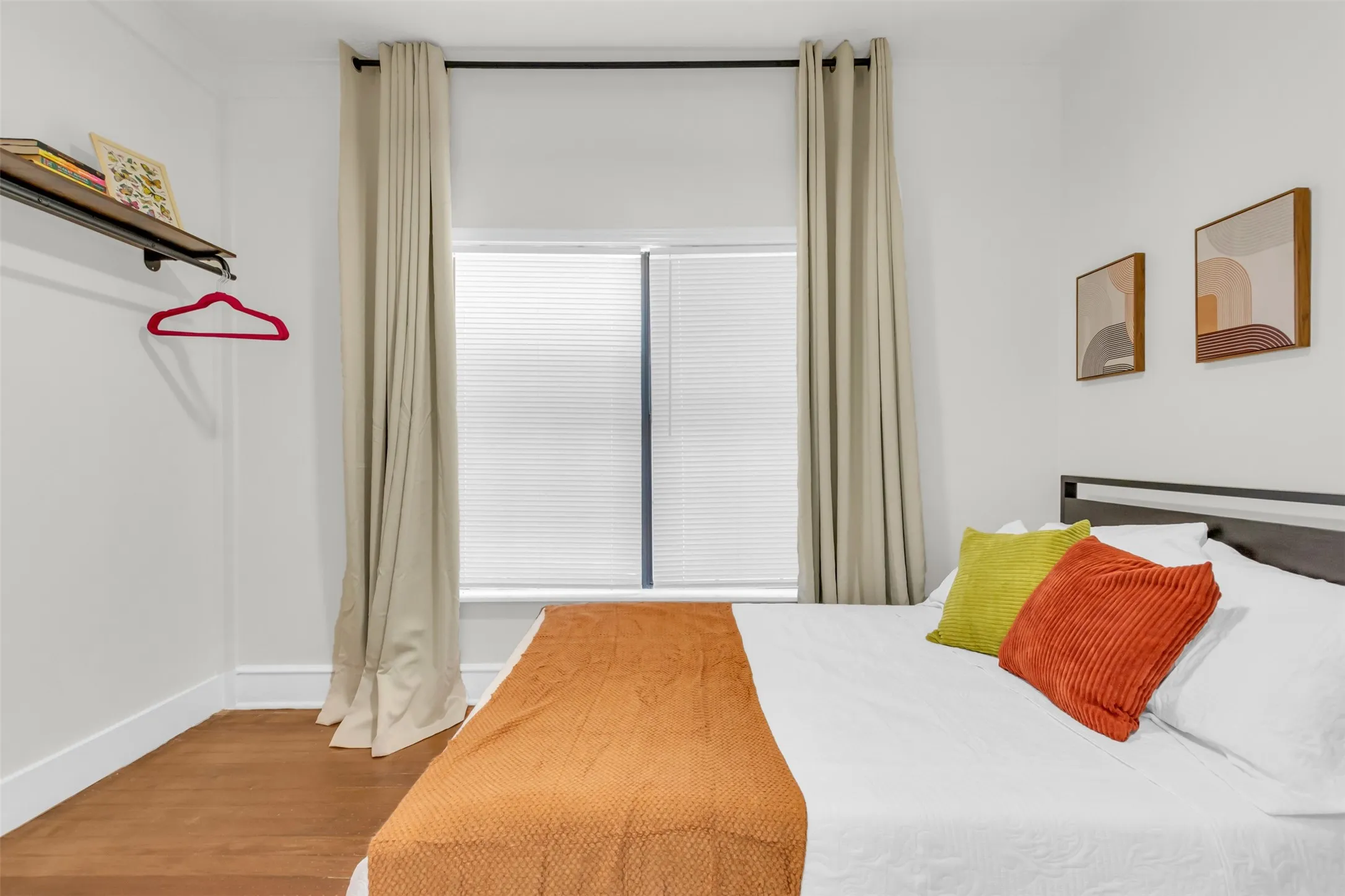 Bedroom featuring wood-finish flooring, white baseboards, and a window with blinds and drapes
