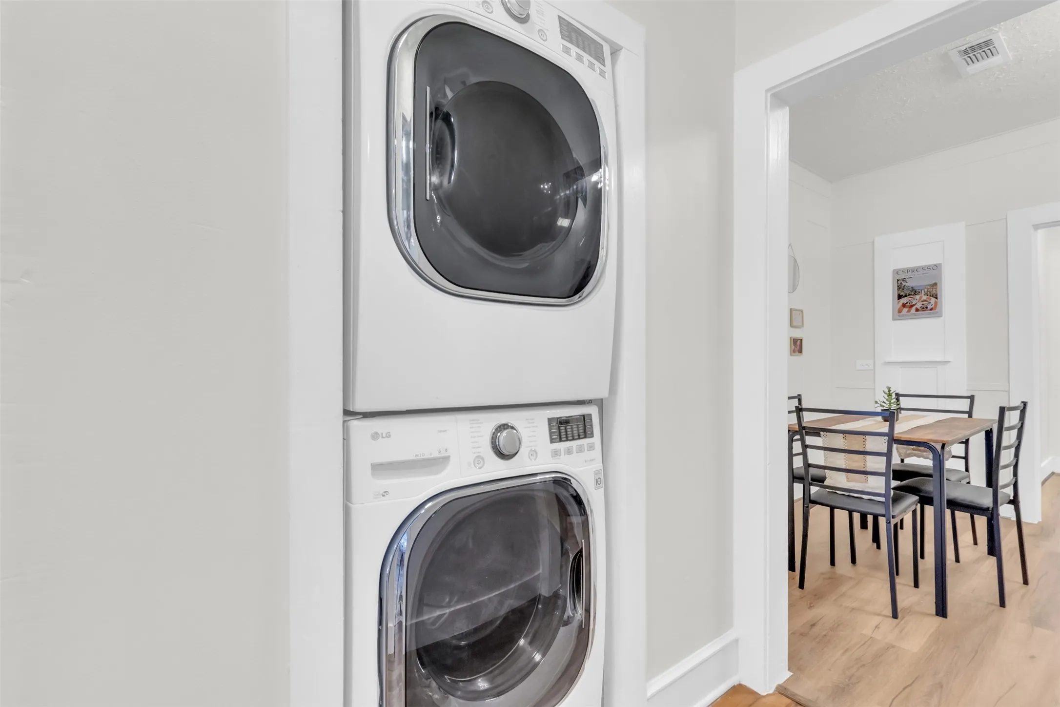Stackable washer and dryer unit with a visible dining area featuring wood-finish flooring