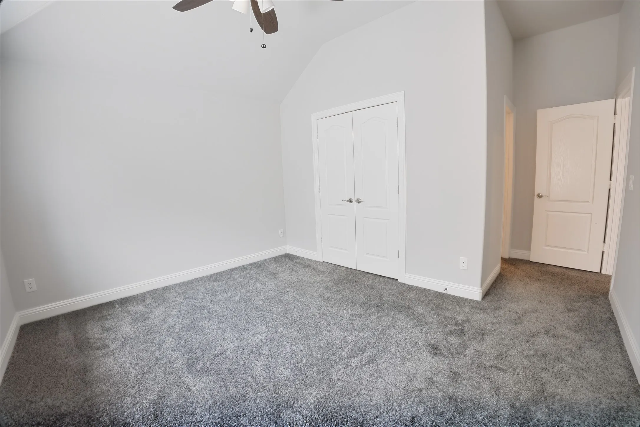 Carpeted room featuring a vaulted ceiling with a ceiling fan, white baseboards, and bright white interior doors