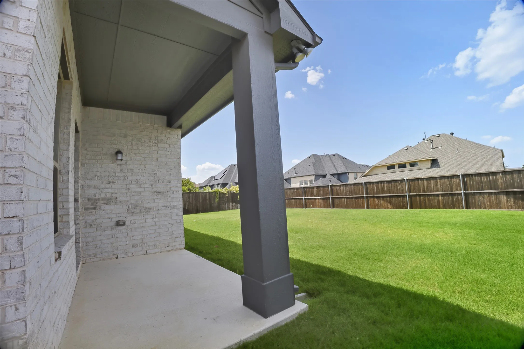Covered patio with a concrete slab, white brick exterior, and a dark-finished support column