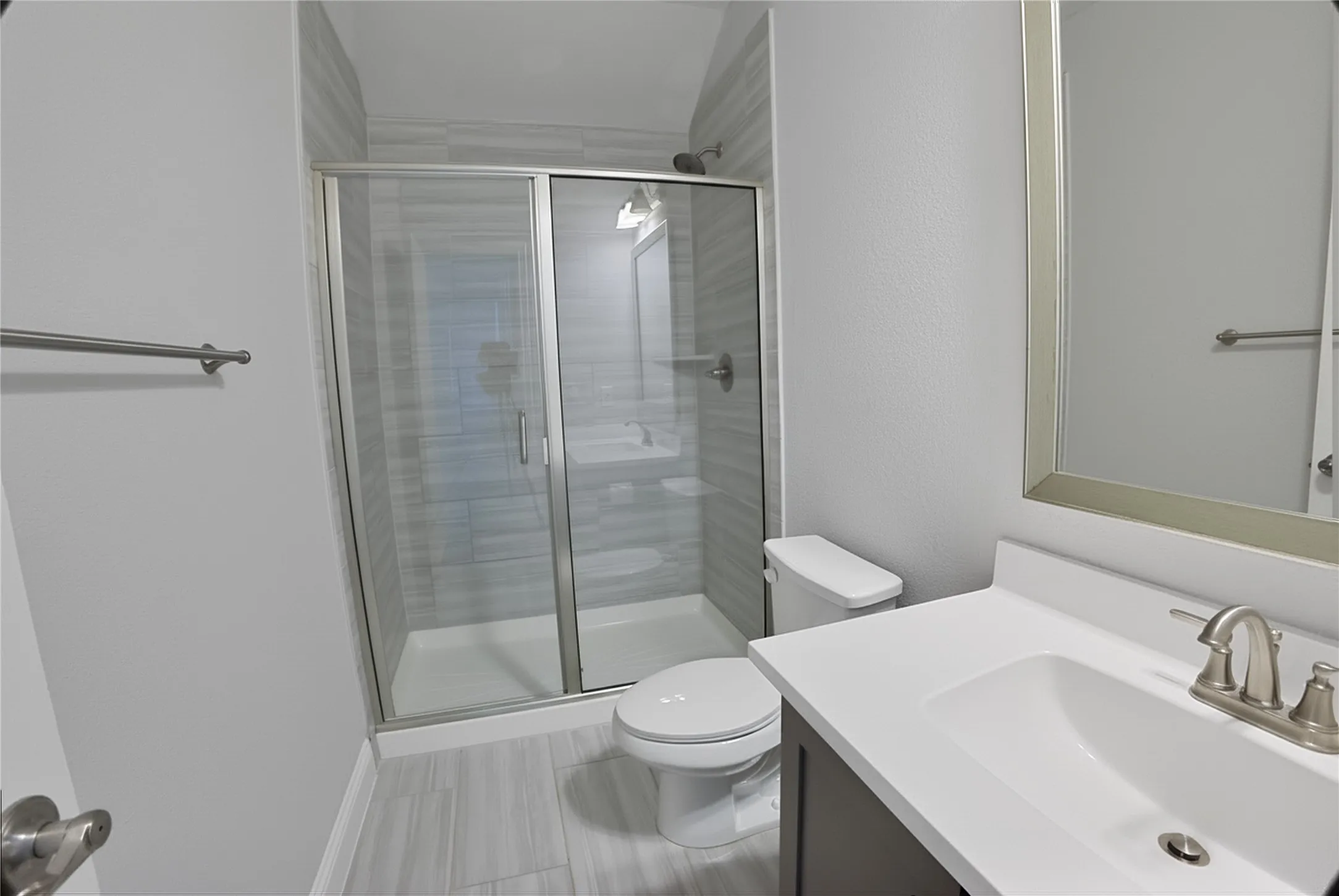 Bathroom featuring a glass-enclosed shower with tile surround, a single vanity with a white countertop and undermount sink, brushed nickel faucet, and a framed mirror