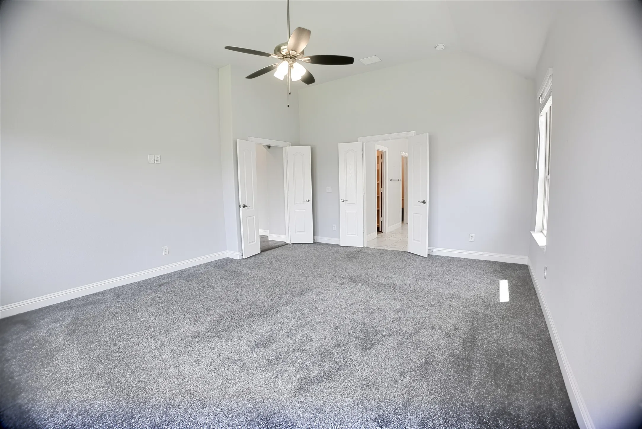 Spacious room featuring vaulted ceilings, a ceiling fan with integrated lighting, plush grey carpeting, and white baseboards