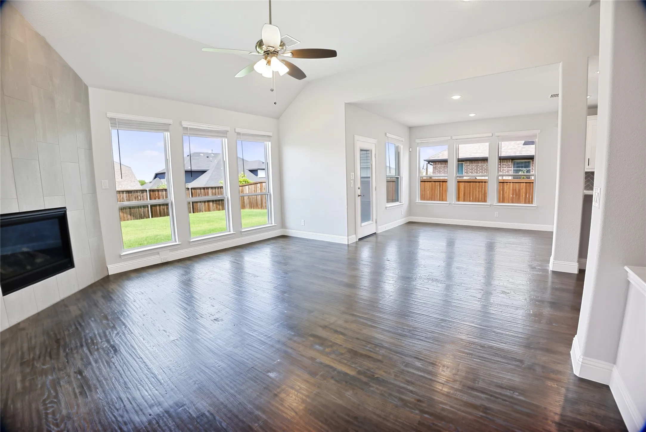 Spacious living area featuring dark wood-finish flooring, a contemporary fireplace with a light-toned tile surround, and an angled vaulted ceiling with a ceiling fan