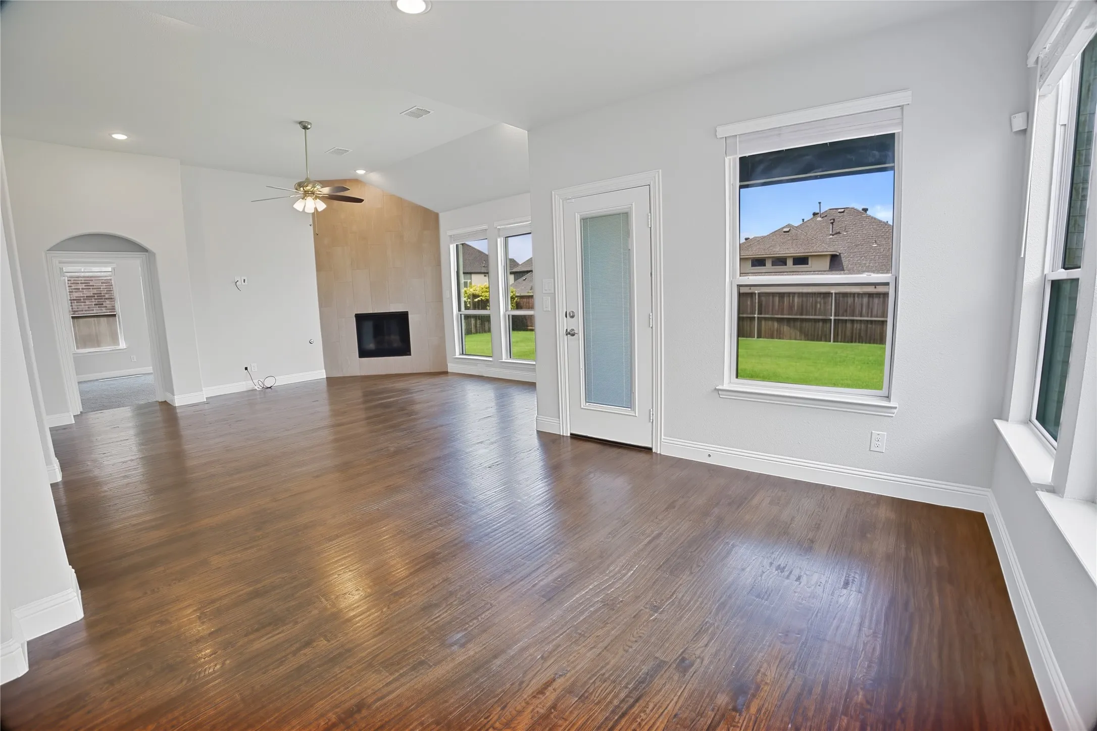 Spacious living area featuring wood-finish flooring, a fireplace with a stone-finish surround, vaulted ceilings, and recessed lighting